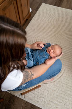 Baby wearing denim overalls sleeping peacefully on parent's lap.