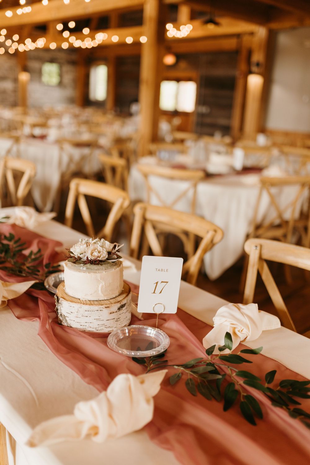 Elegant wedding table with dusty rose runner, mini cake on birch slice, and table number 17 card.