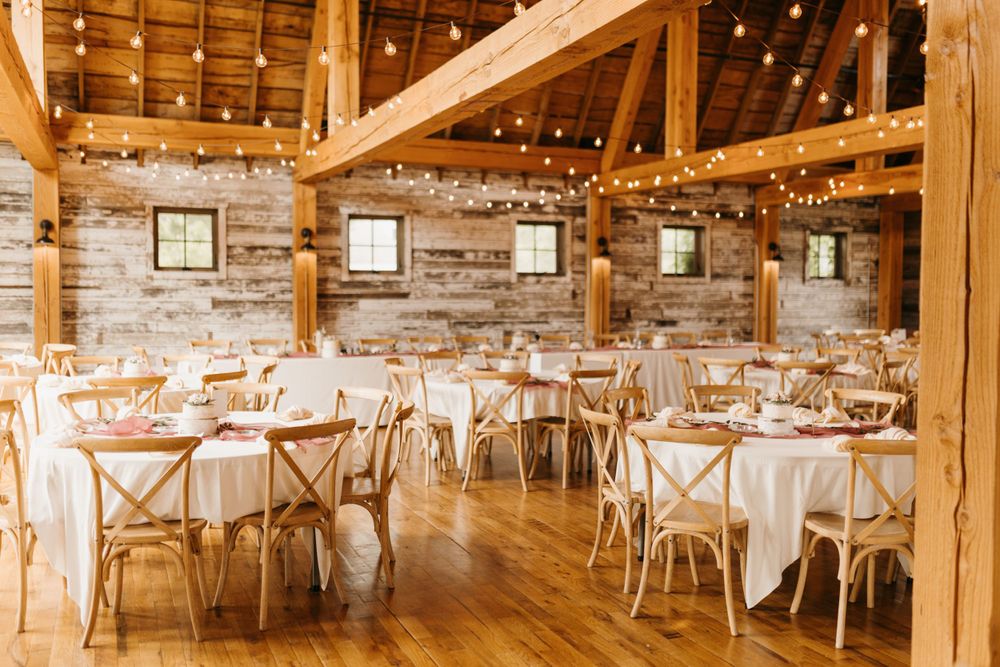 Rustic barn wedding reception with string lights, white linen tables, and natural wood cross-back chairs.