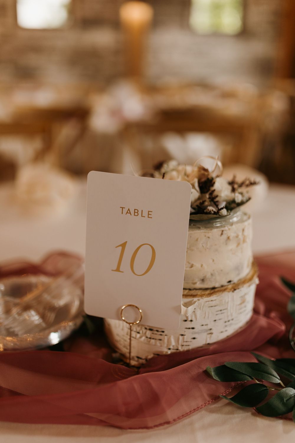 Gold table number 10 card displayed on a birch wood slice with dusty rose gauze runner.