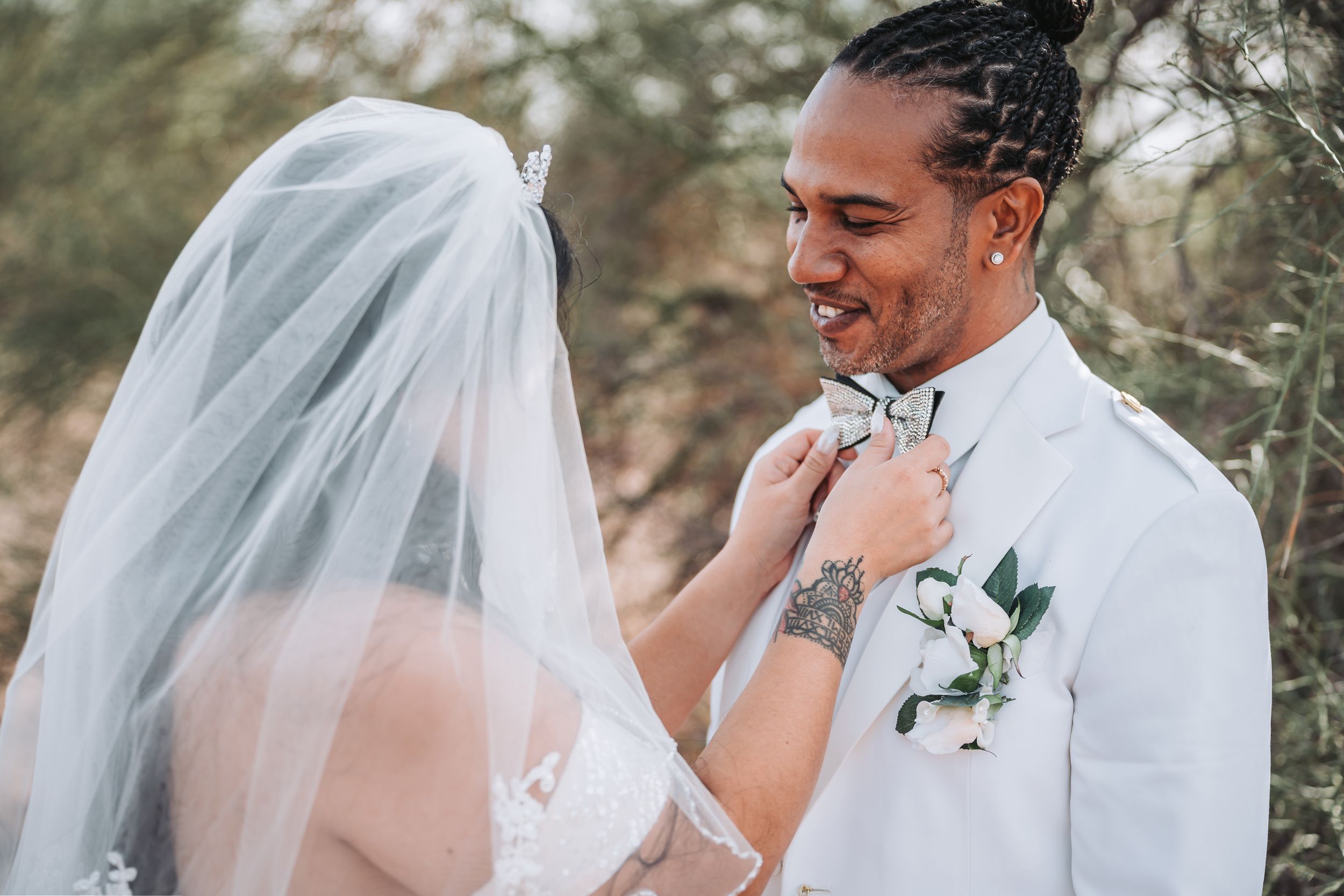 A tender moment between a bride and groom in white attire during their outdoor desert wedding ceremony.