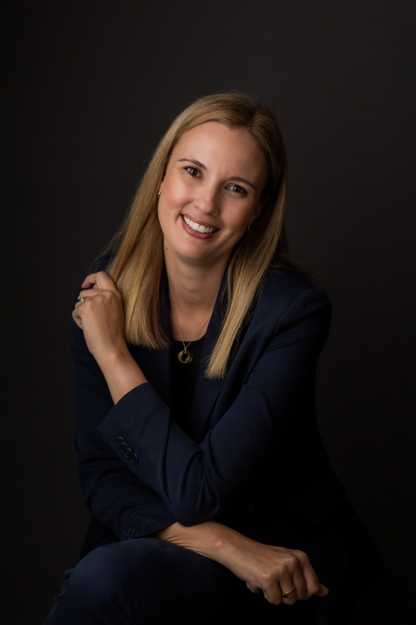 Chenara Evans smiling at the camera with navy blue suit on a black background shot by Stela McMillan in Dubai.