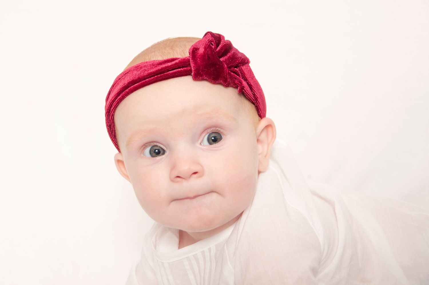 Seven month old girl with headband on white backdrop indoor photo session