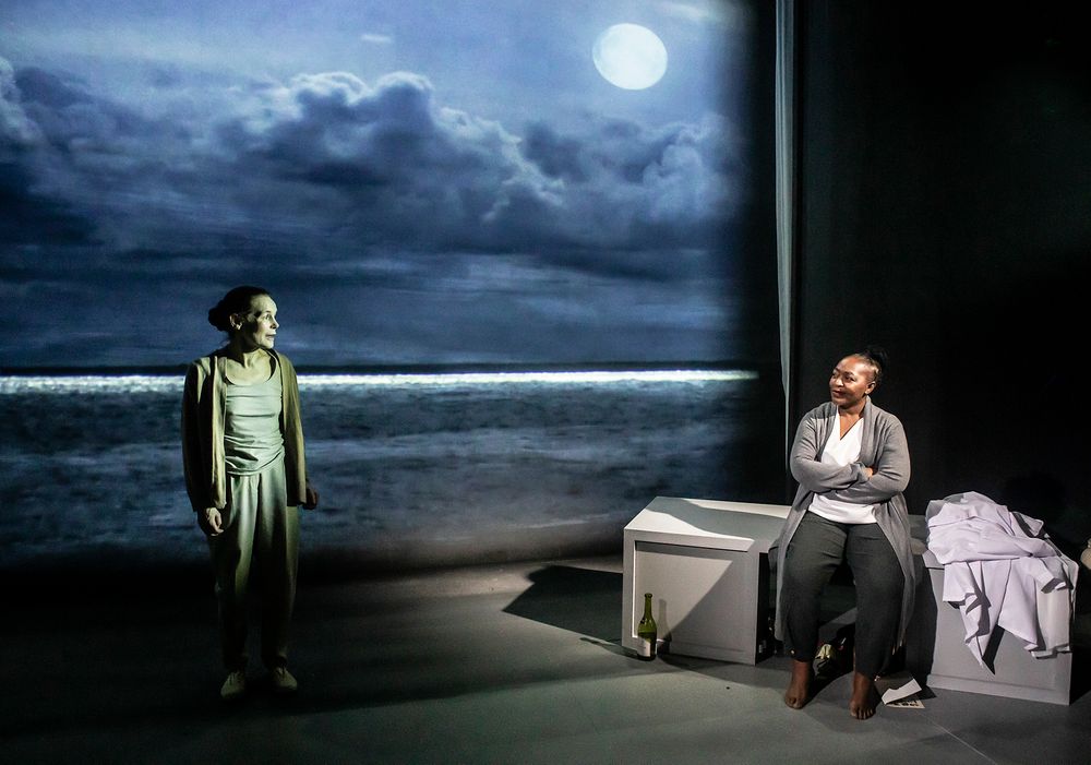 Two actors perform in a moonlit beach scene with dramatic lighting on a theatrical stage.