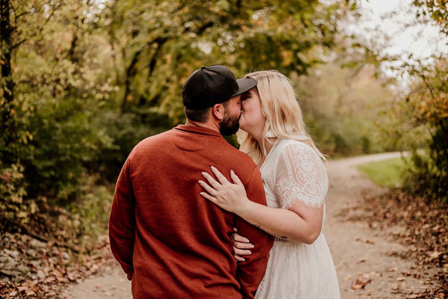 Romantic couple embracing on autumn path surrounded by fall foliage.