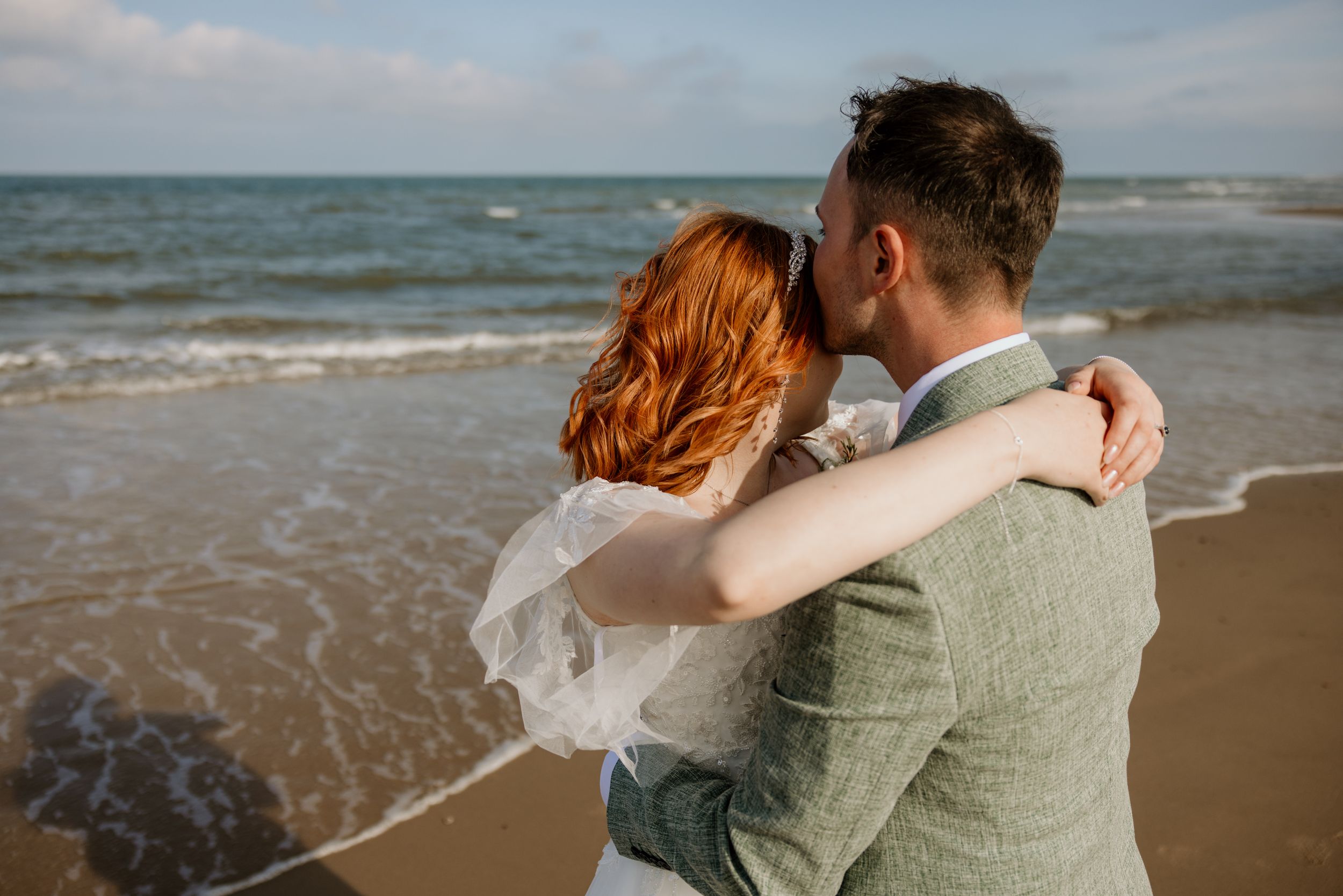bride and groom with there arms around each other on their beach, with the sea