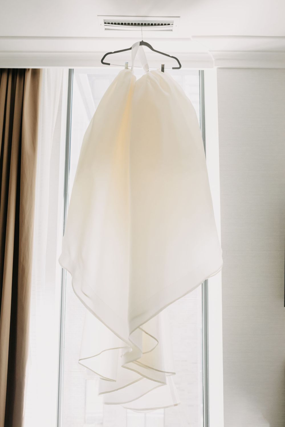 White wedding dress hanging in front of window with soft natural light.