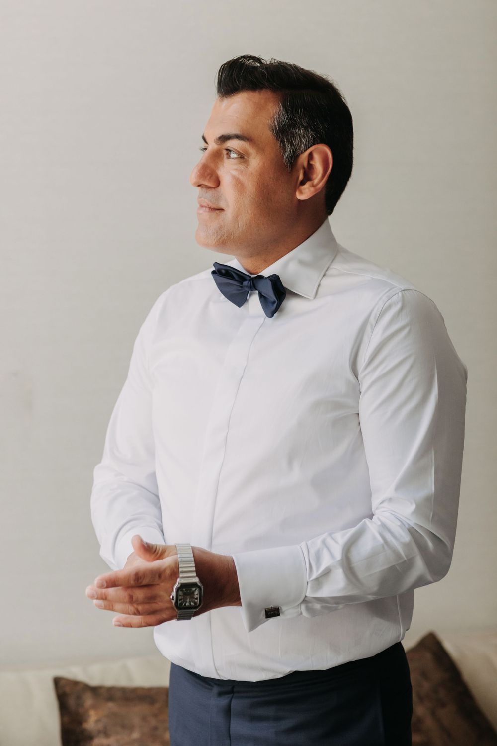 Side profile of groom in white shirt and navy bow tie preparing for wedding.