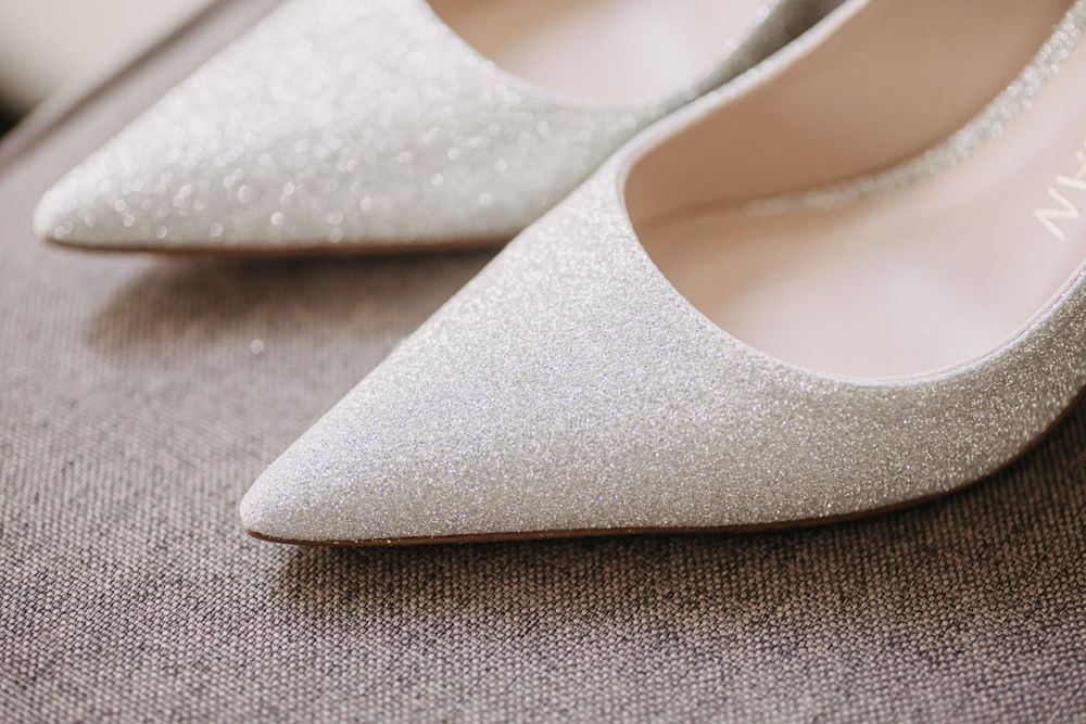 Sparkly white pointed-toe bridal shoes on grey fabric.