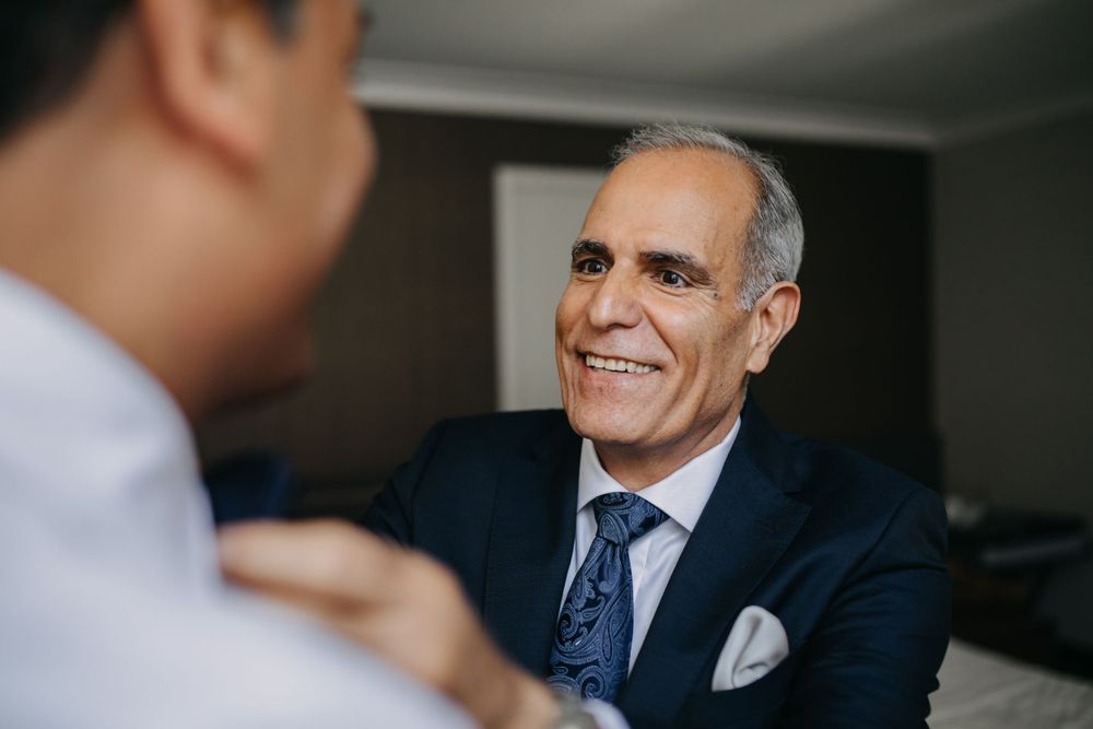 A man in a navy suit and tie smiles during a conversation.