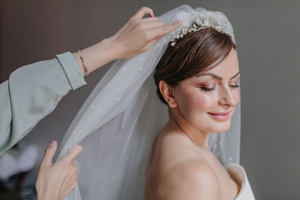 A wedding veil is being adjusted on a bride wearing an elegant tiara and white dress.