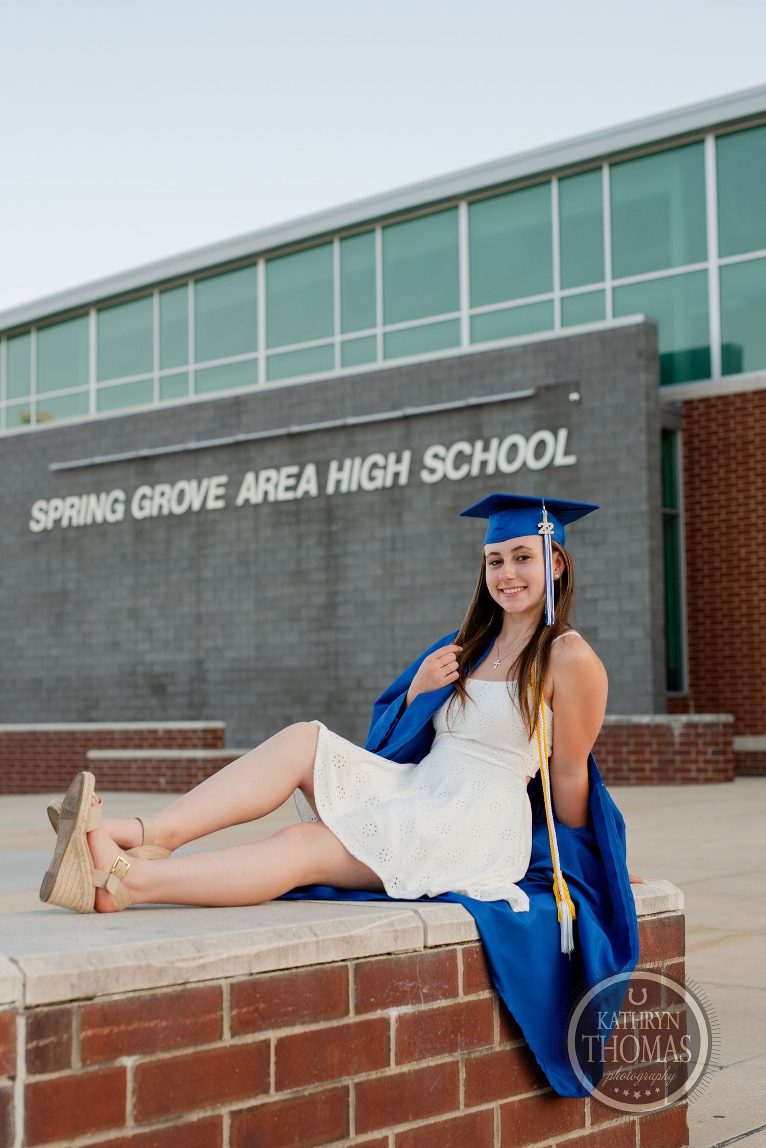 Graduate relaxes on brick wall outside Spring Grove Area High School in graduation attire.