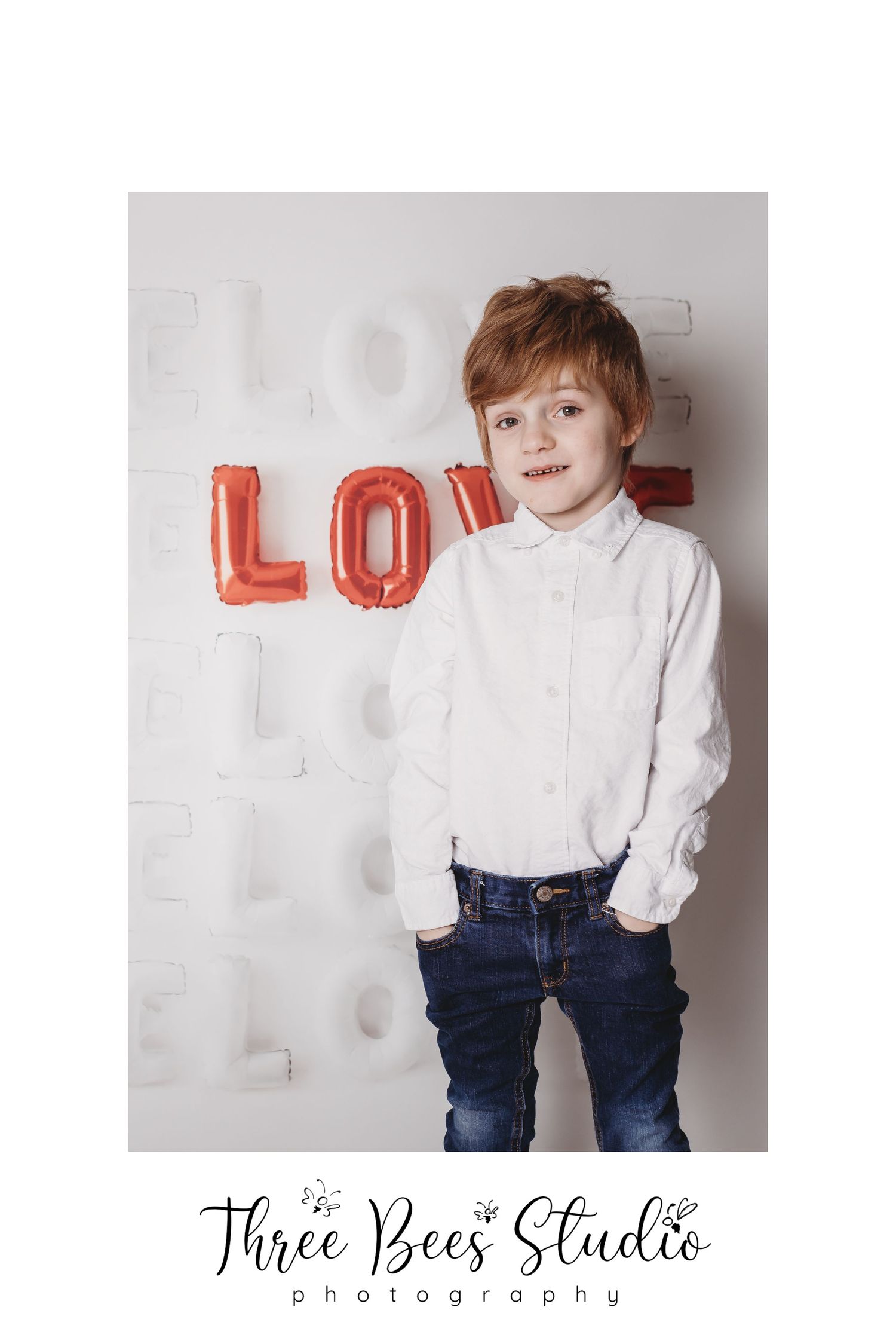 Portrait of child in white shirt against textured wall with red love balloon letters.