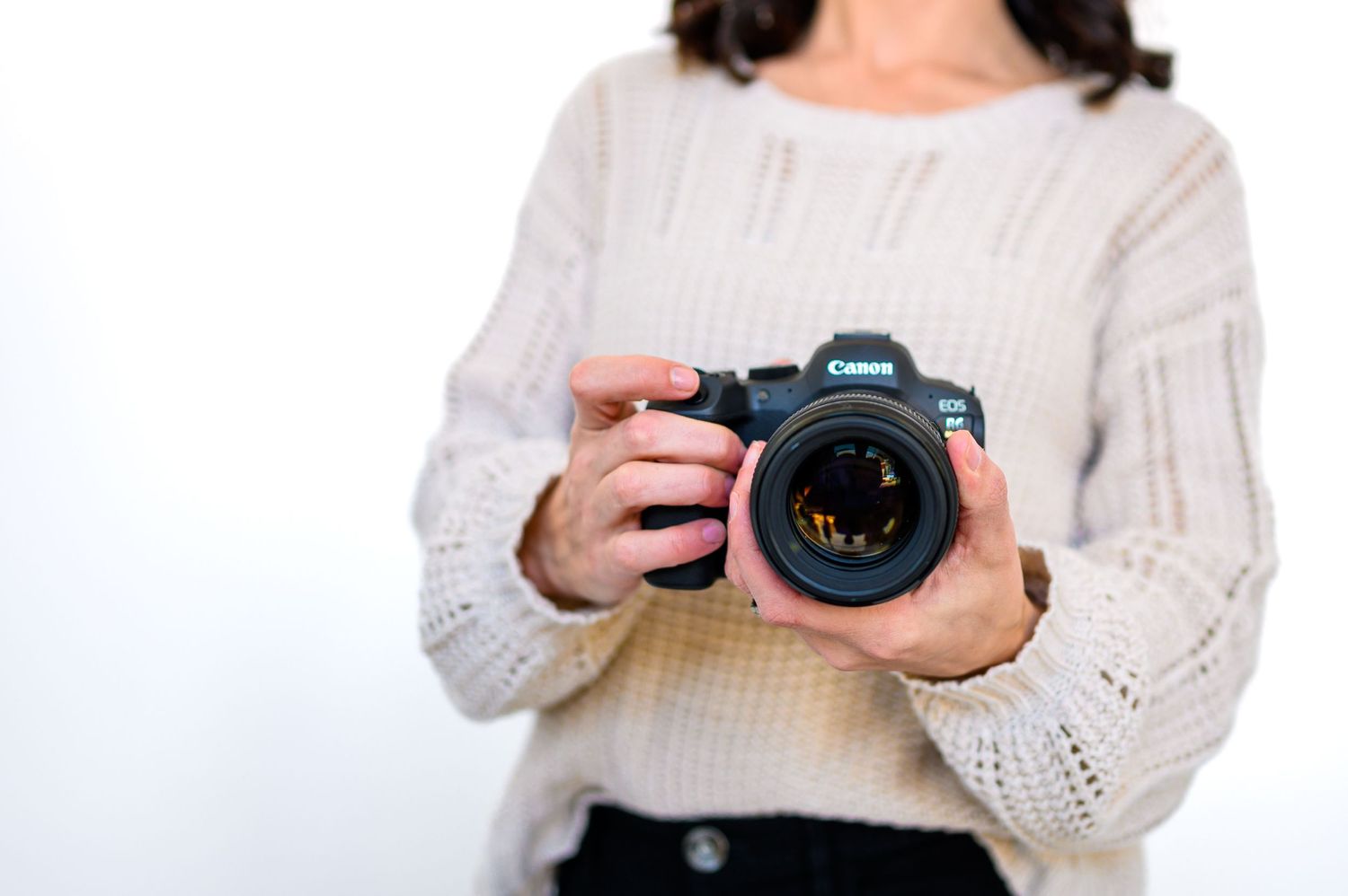 A close up of a photographer's black camera being held by a woman in a tan sweater.