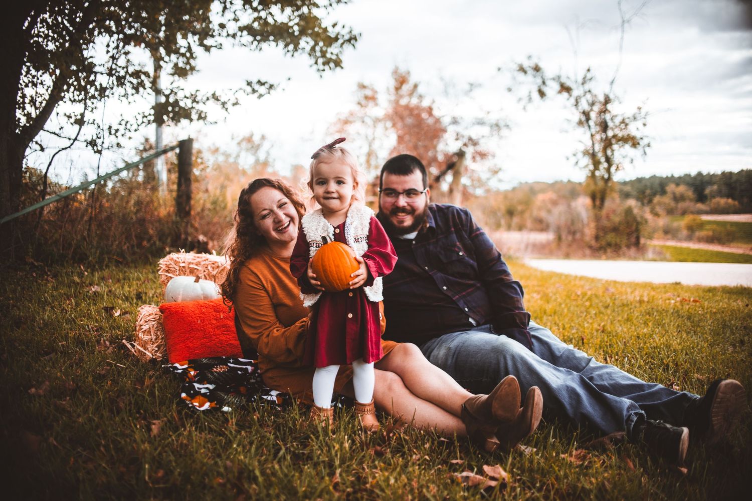 A happy family sitting together on autumn grass with fall colors in the background.