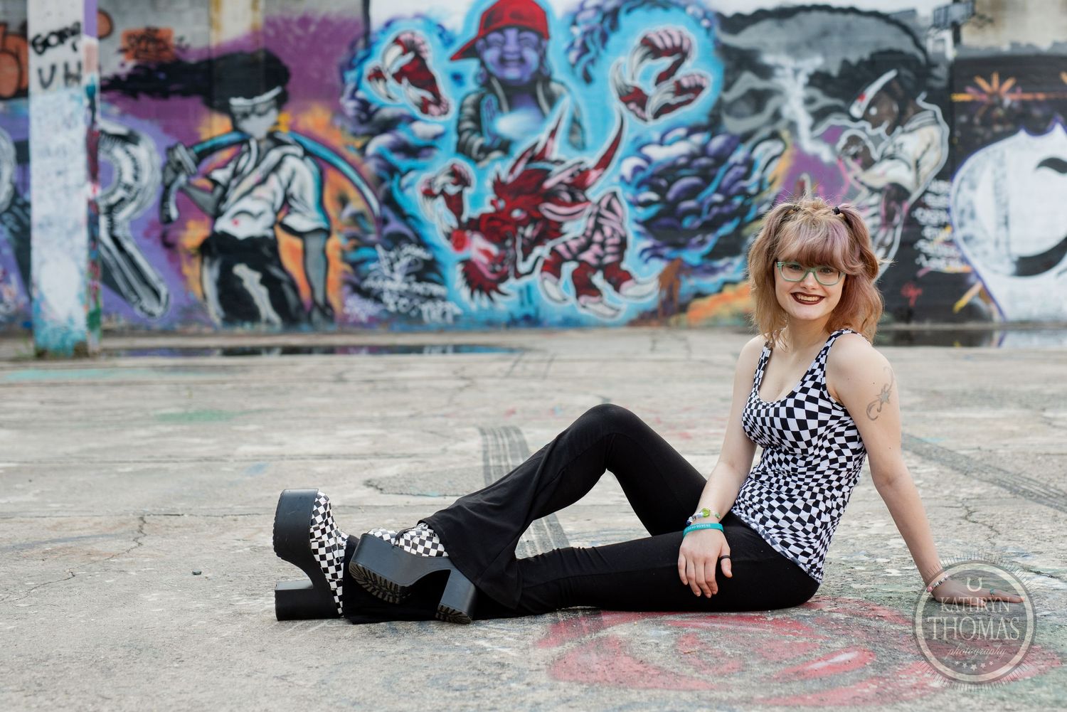 A casual pose on concrete floor with colorful graffiti background and checkered outfit.