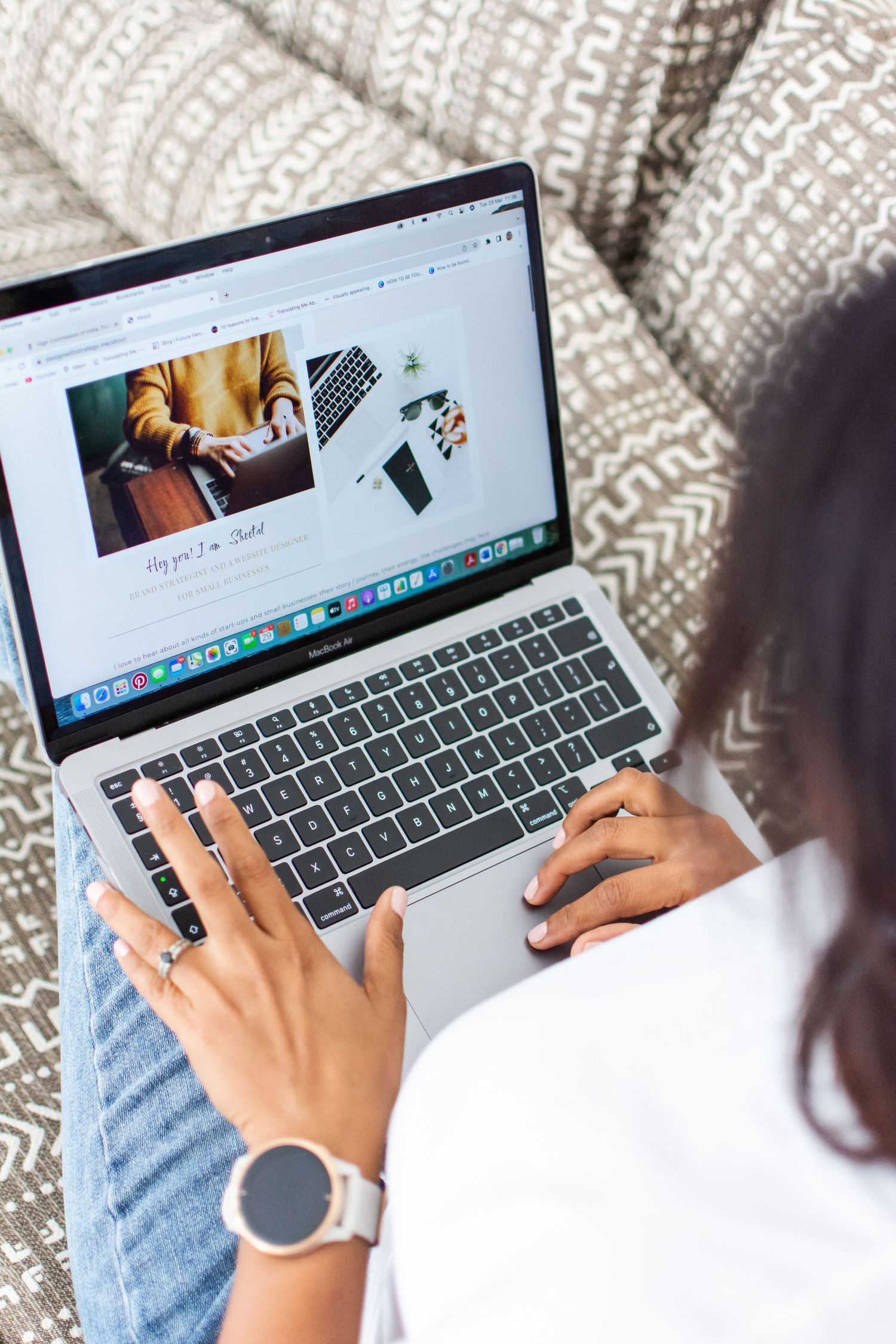 Person working on laptop showing website design with cozy textured pillows in background.