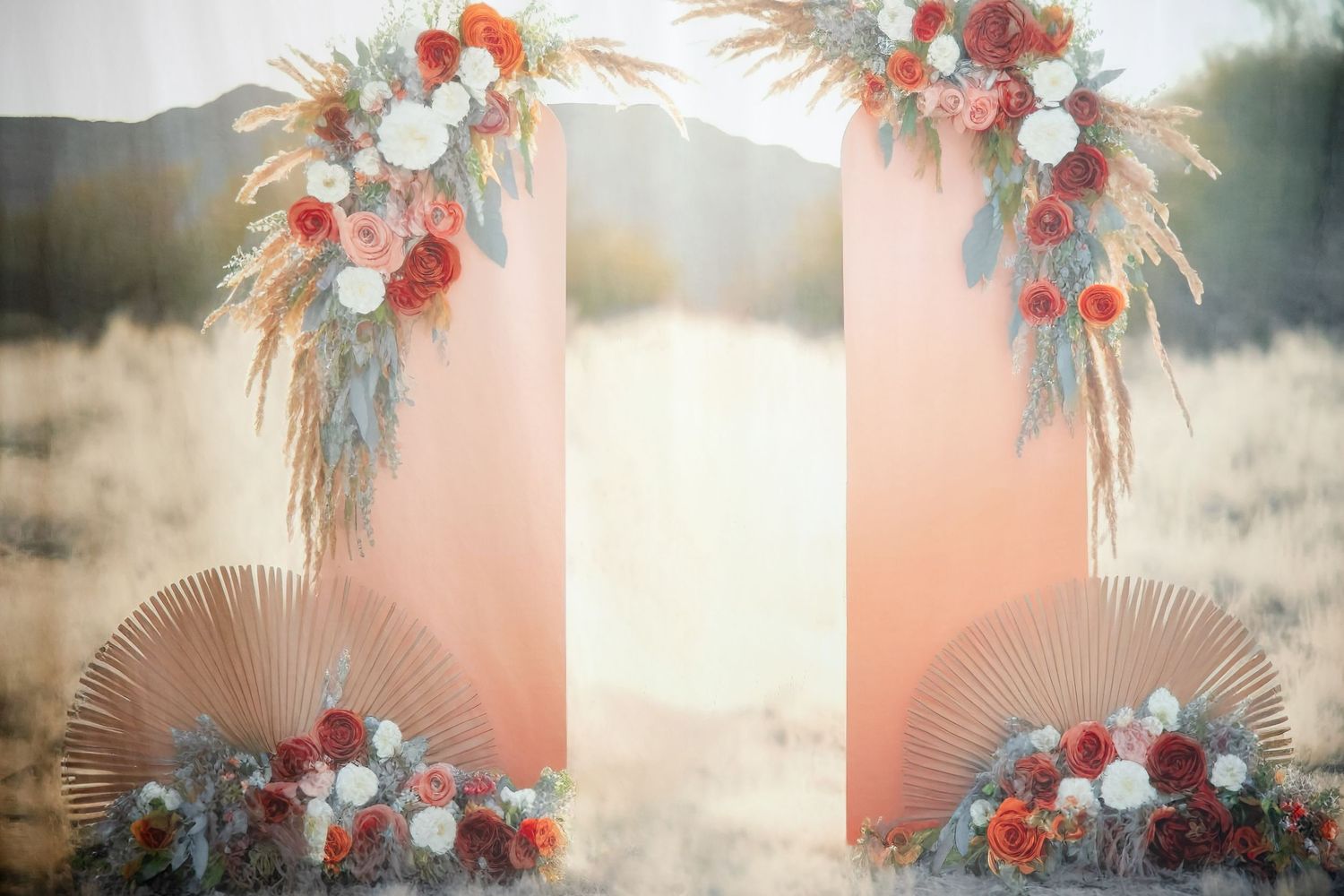 Wedding arch decorated with dried pampas grass and floral arrangements against a sunset backdrop.