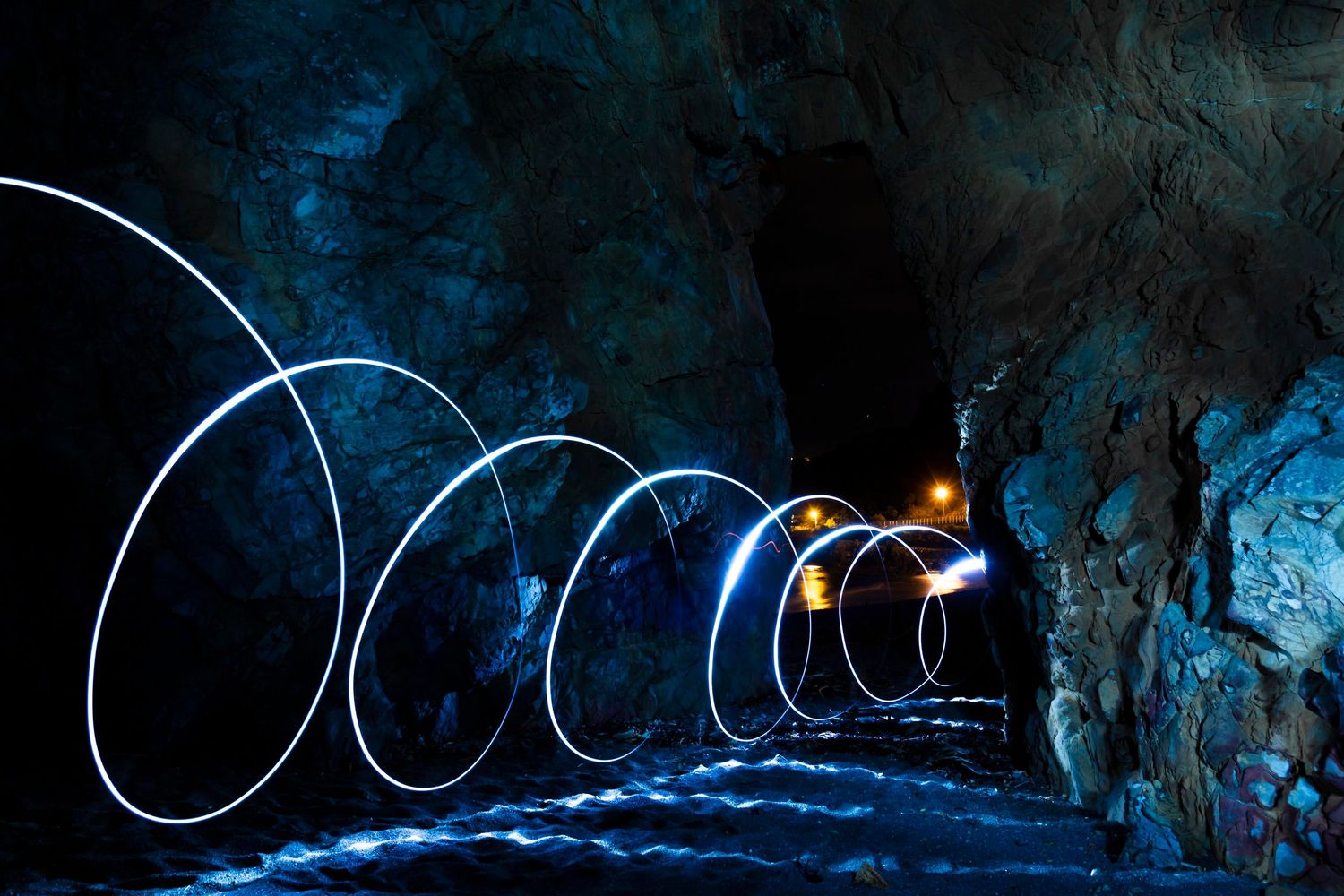 Spirals of light dance through a dark cave tunnel, illuminating the rugged walls with electric glow.