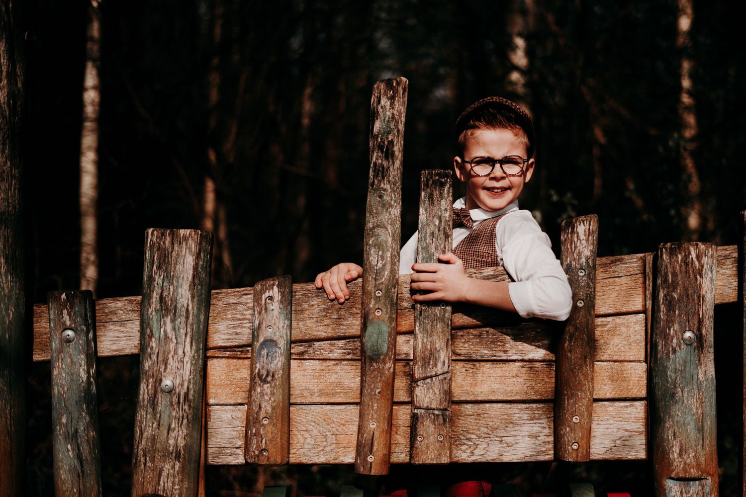 Een kind gluurt door houten schuttingpalen in een rustieke bosomgeving.