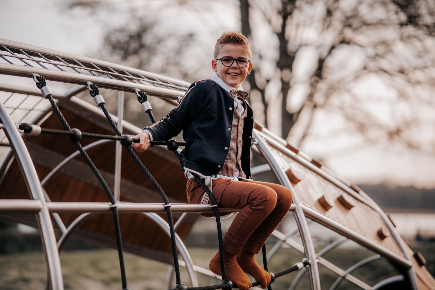 Kind in formele kleding speelt op geometrische klimstructuur bij zonsondergang.