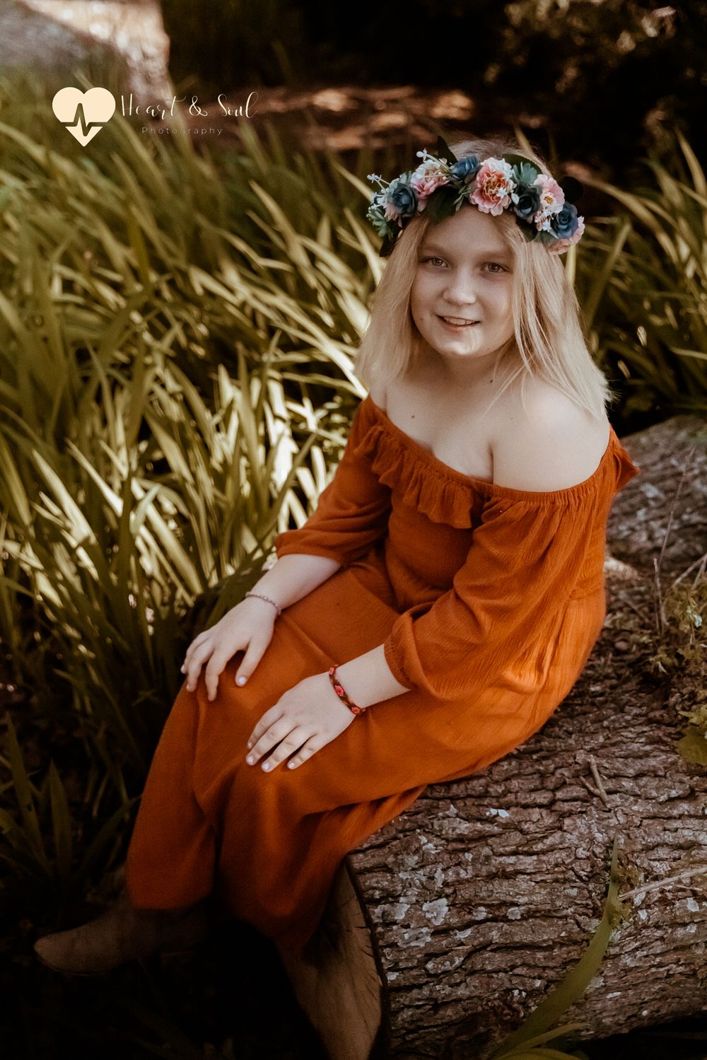 girl dressed in orange with flower headband sitting on log