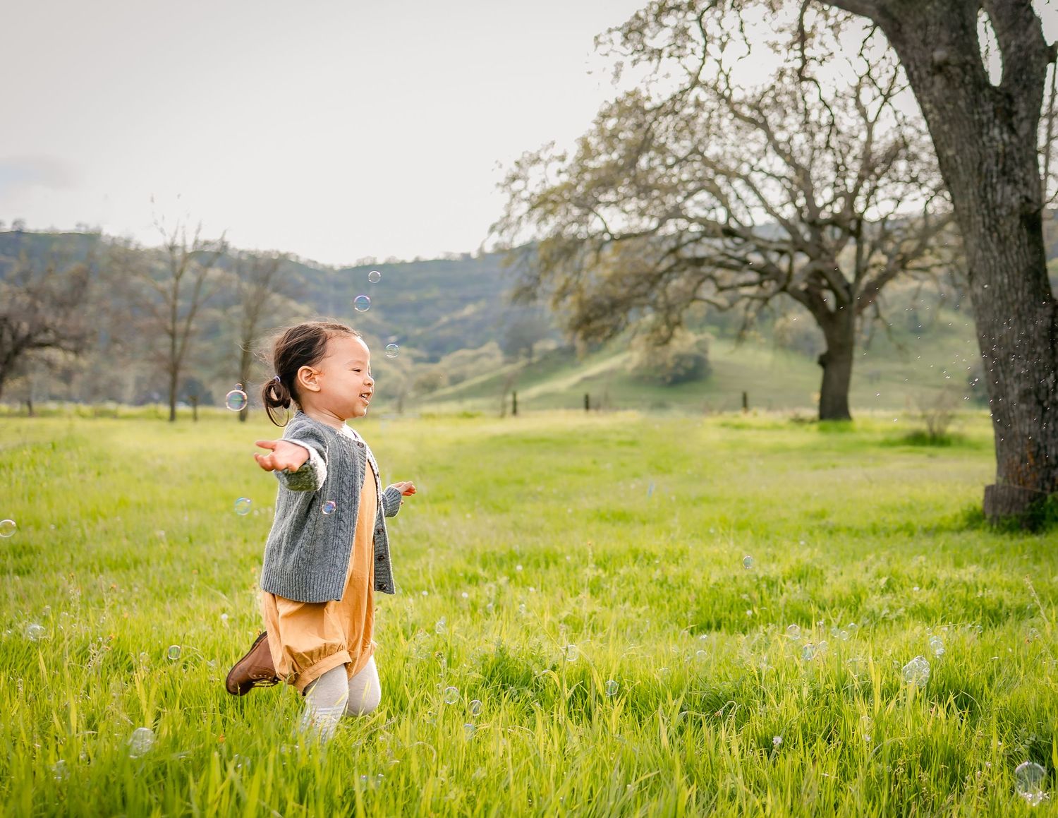 Toddler girl runs in flower field, chasing bubbles