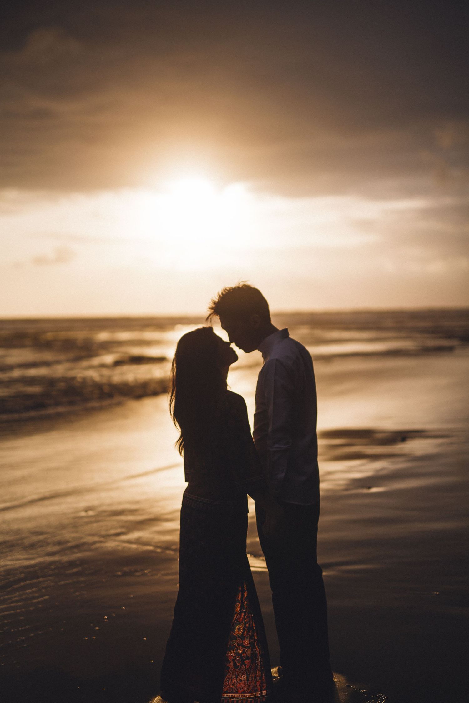 Romantic sunset beach portrait with couple in silhouette against golden sky.