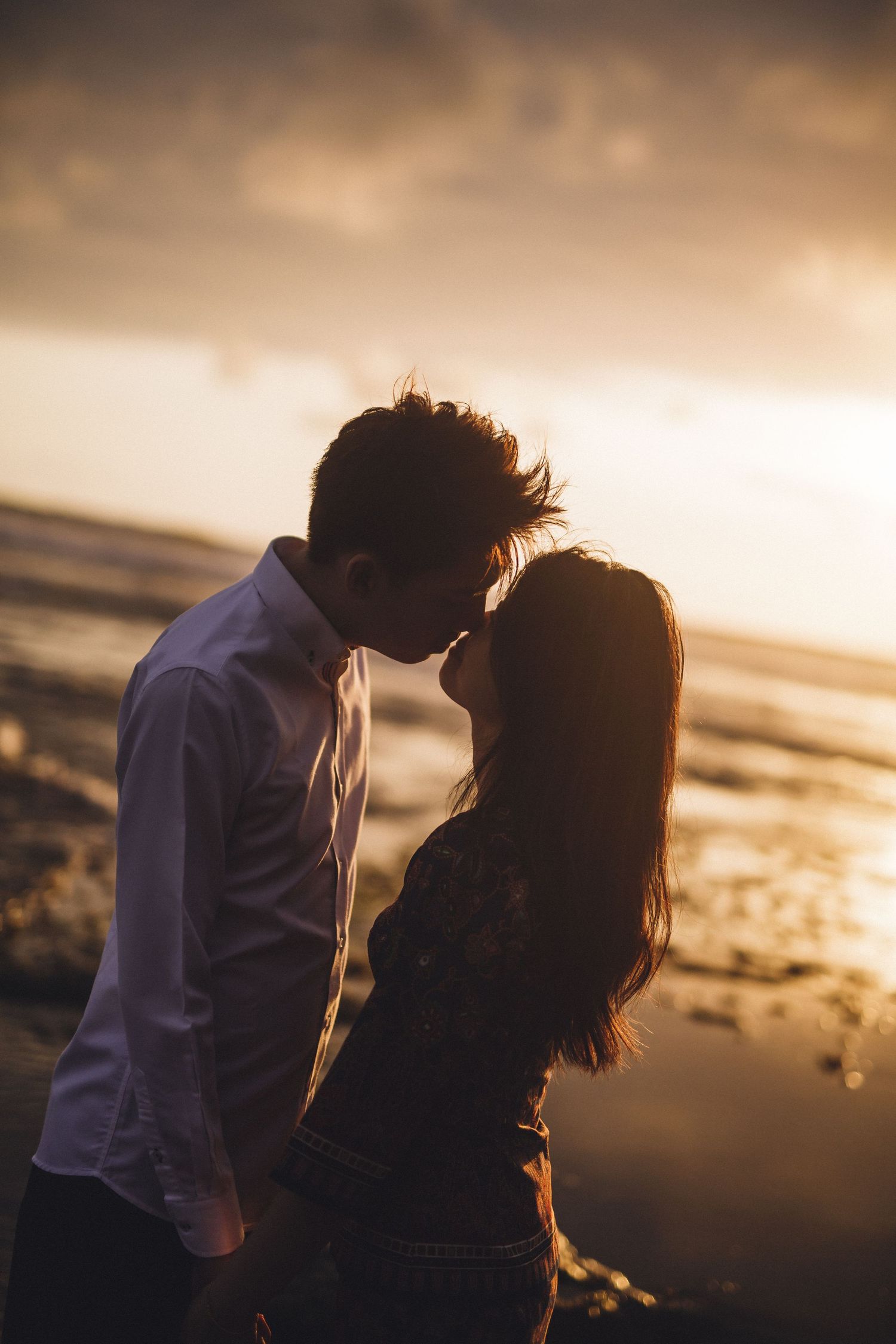 Silhouetted couple sharing an intimate moment against a dramatic sunset on the beach.