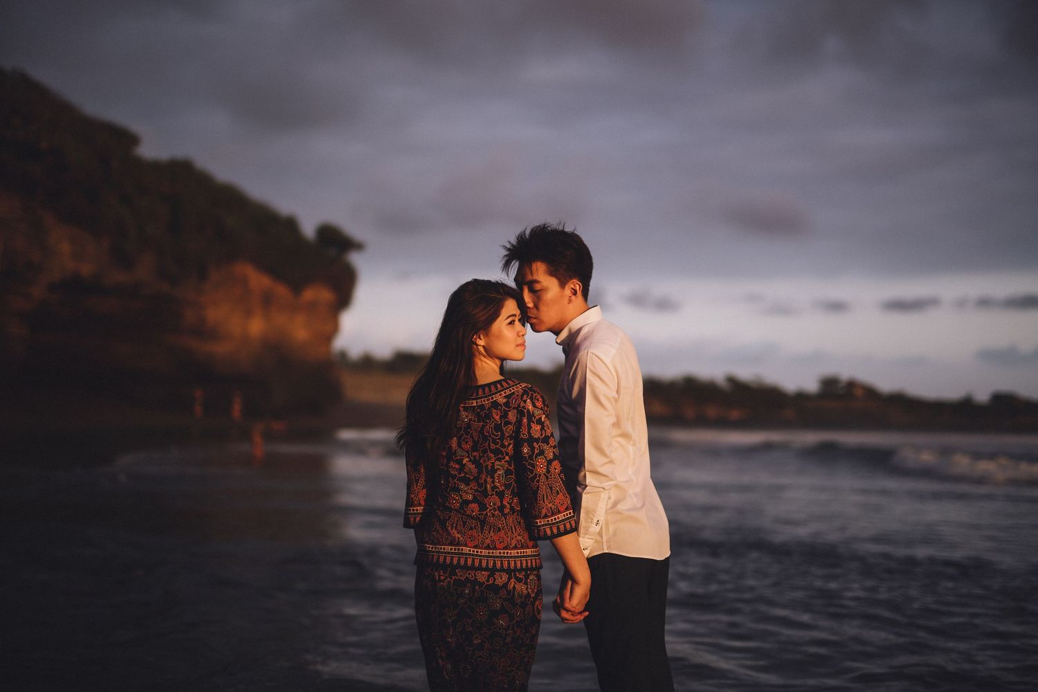 Romantic beach photoshoot with dramatic coastal cliffs and moody skies in the background.