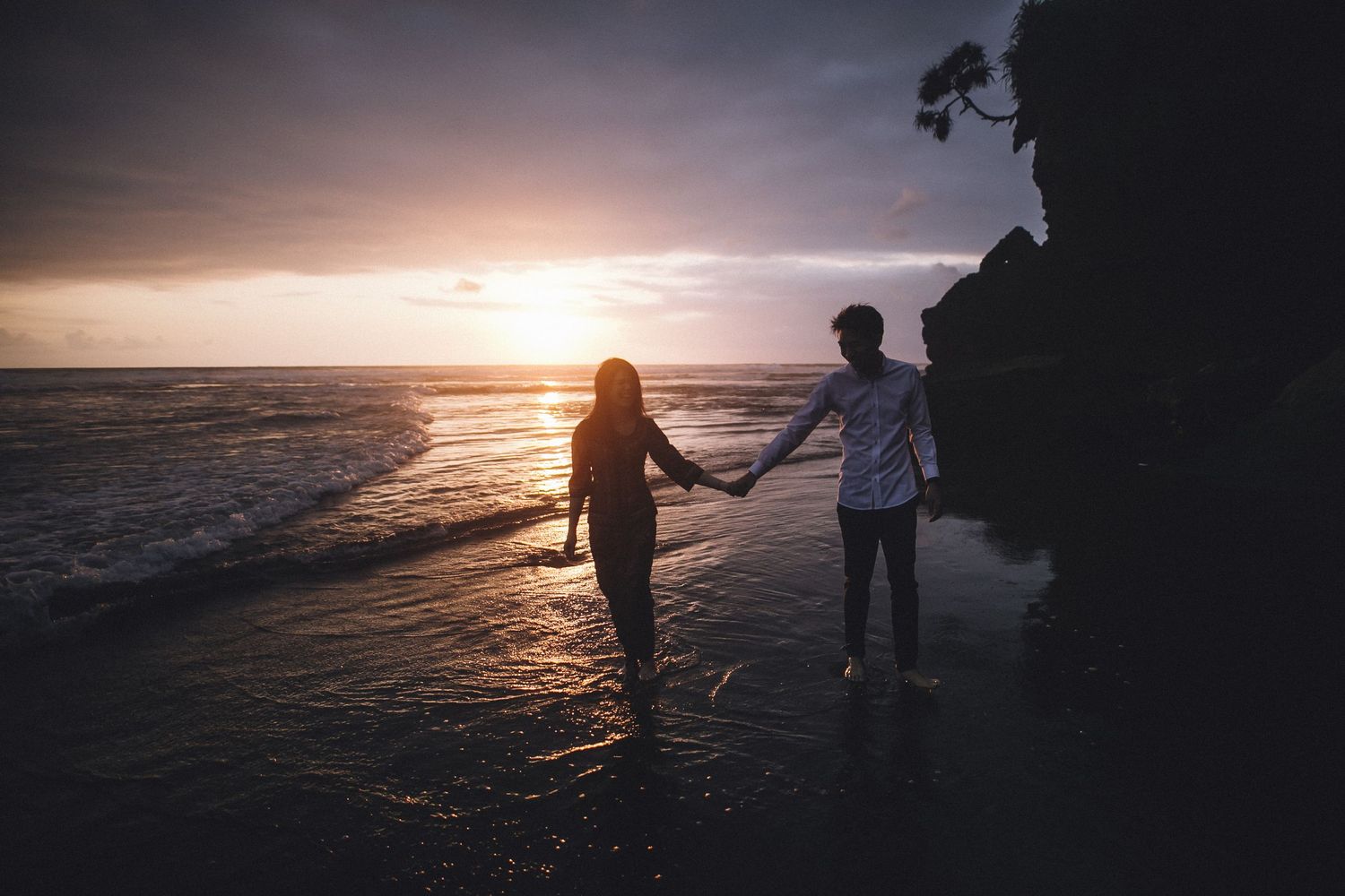 Silhouettes walking on beach during golden hour with dramatic ocean backdrop.