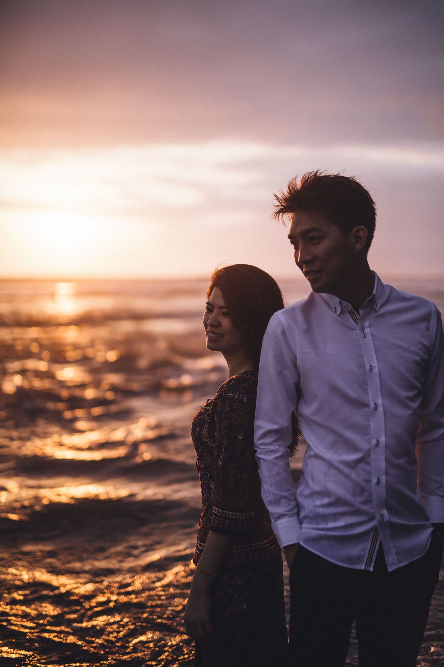 Couple on beach during golden hour with dramatic ocean waves and sunset.