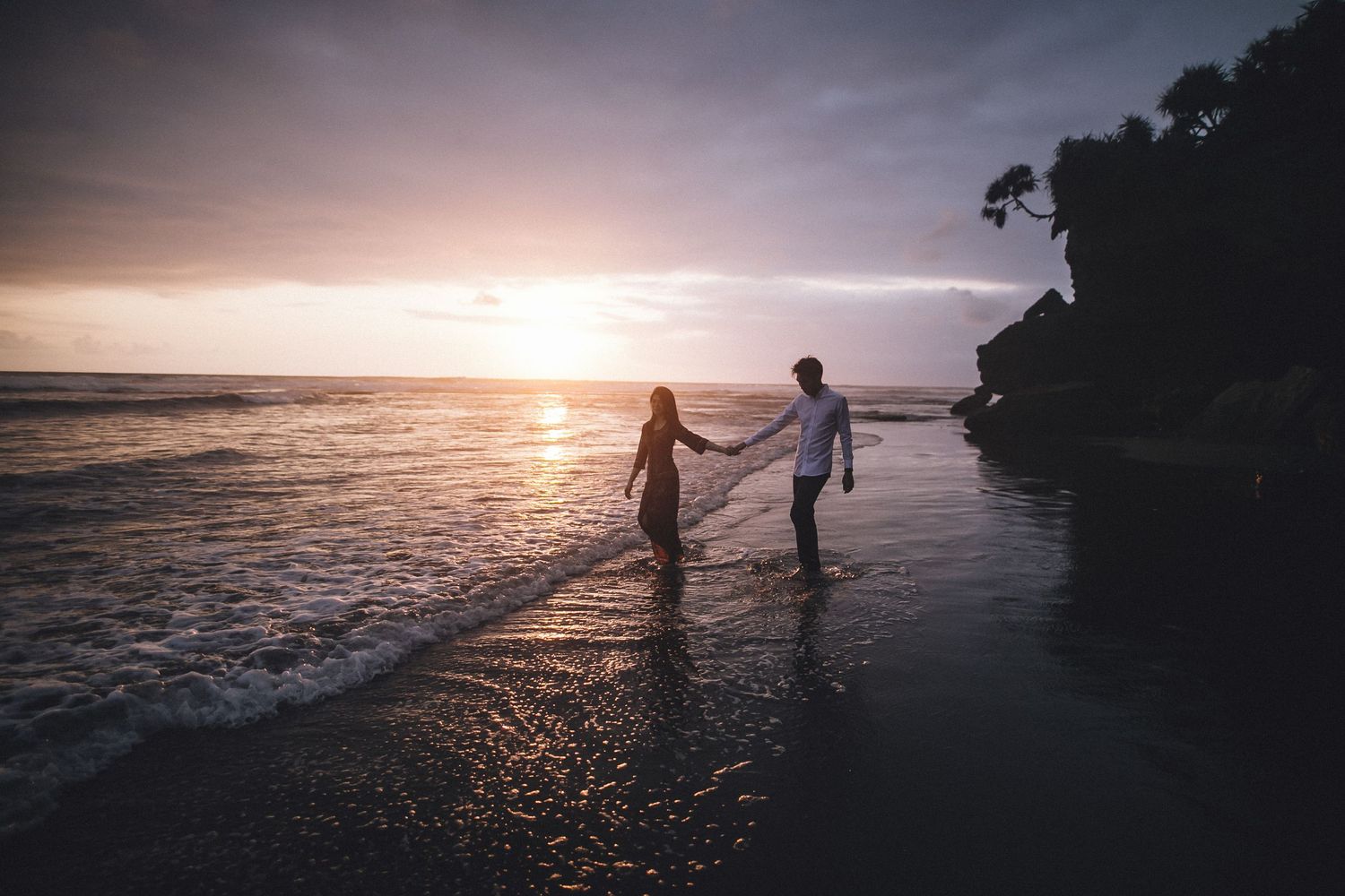 Wide angle shot of beach sunset with silhouettes walking along shoreline.