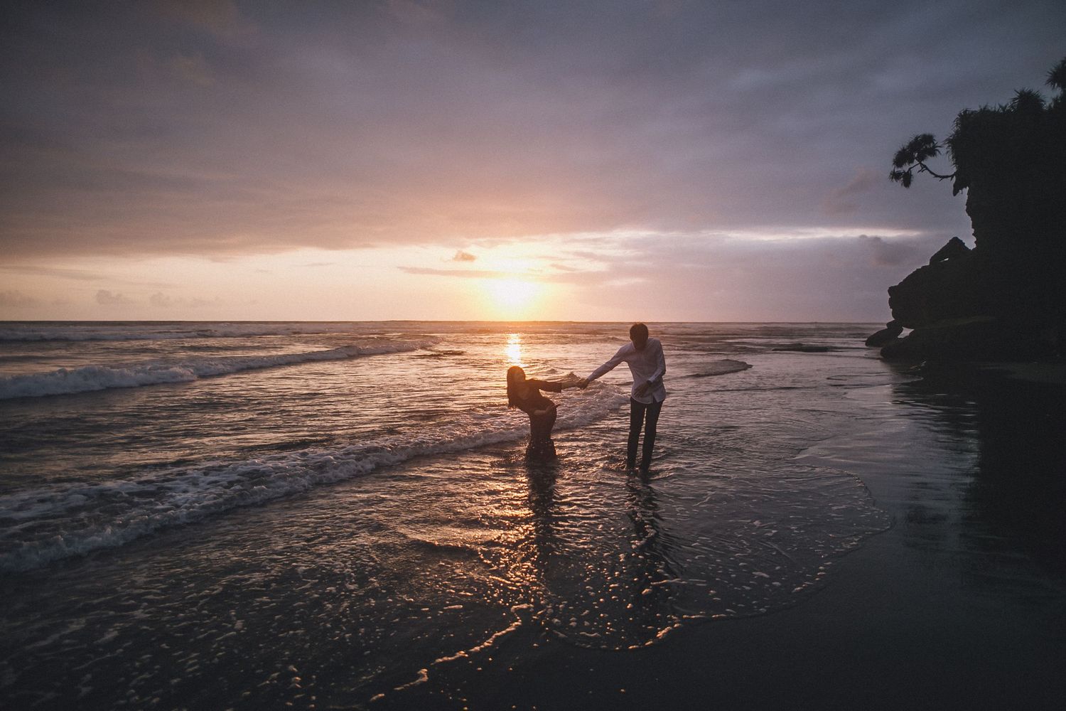Panoramic beach scene with silhouettes against setting sun and coastal cliffs.