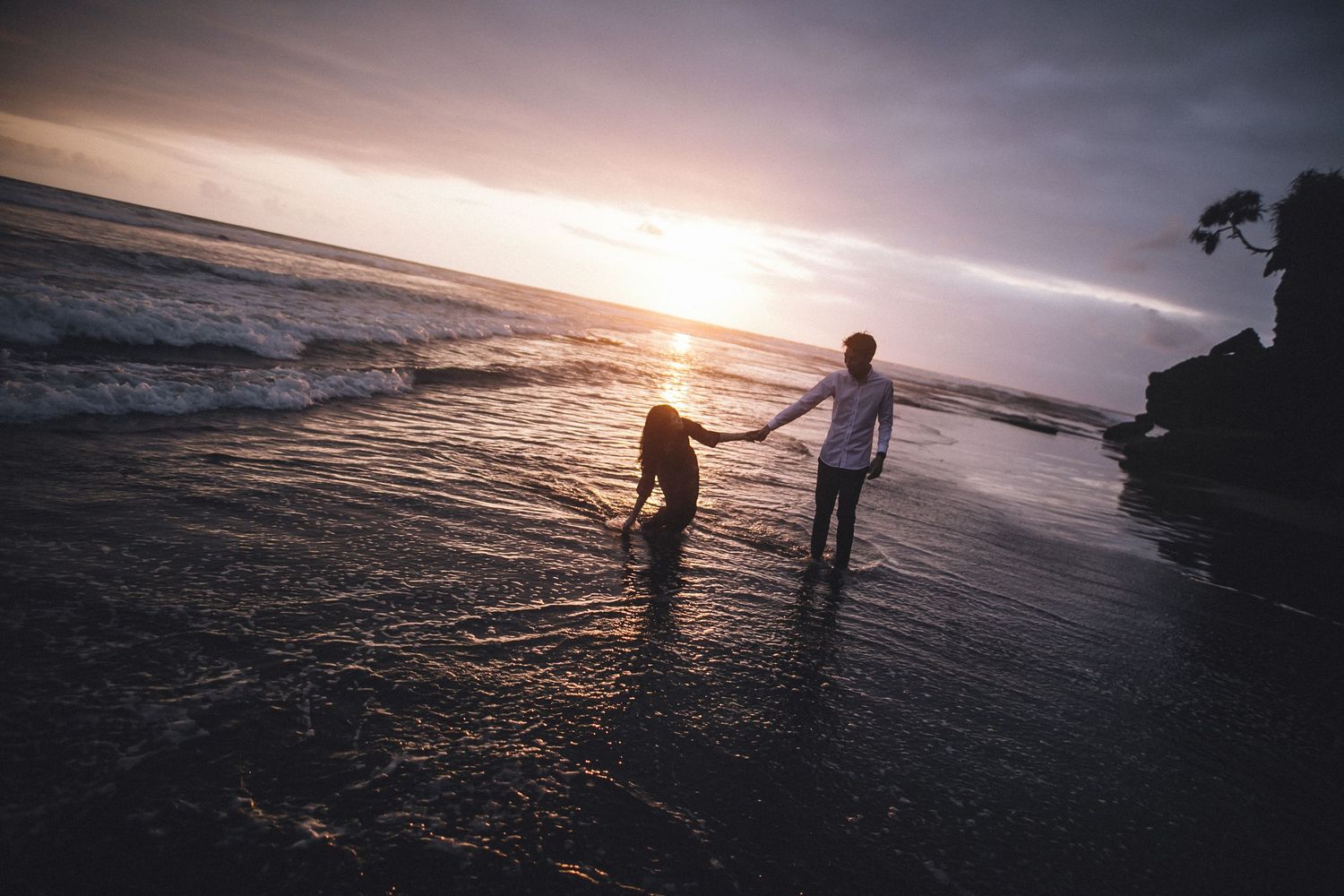 Wide coastal landscape with figures walking along shoreline during sunset.