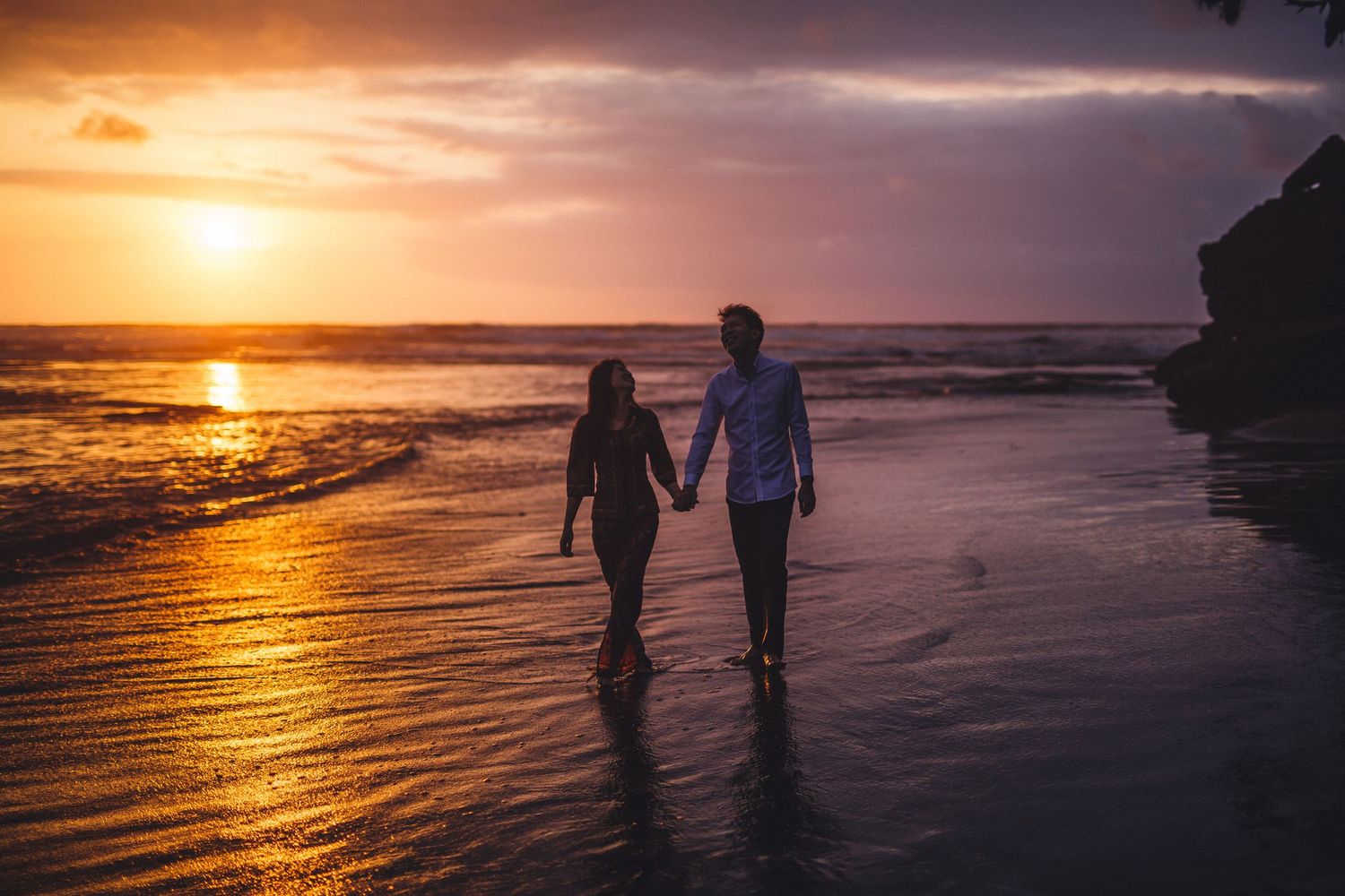 Panoramic view of two figures walking on a golden beach during a vibrant sunset.