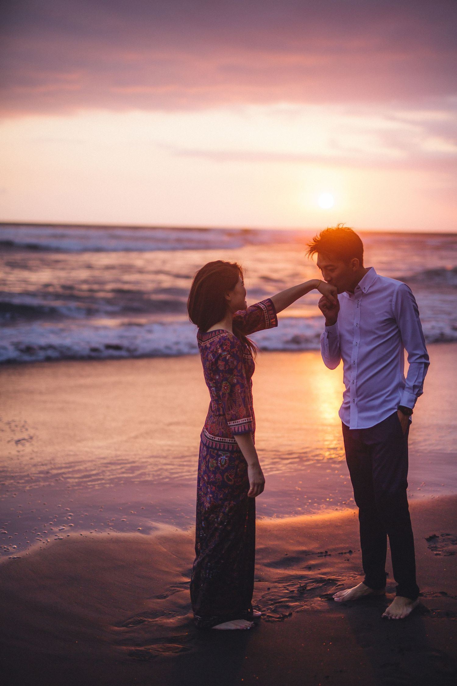 A couple dancing together on the beach at sunset with orange sky reflecting on the water.