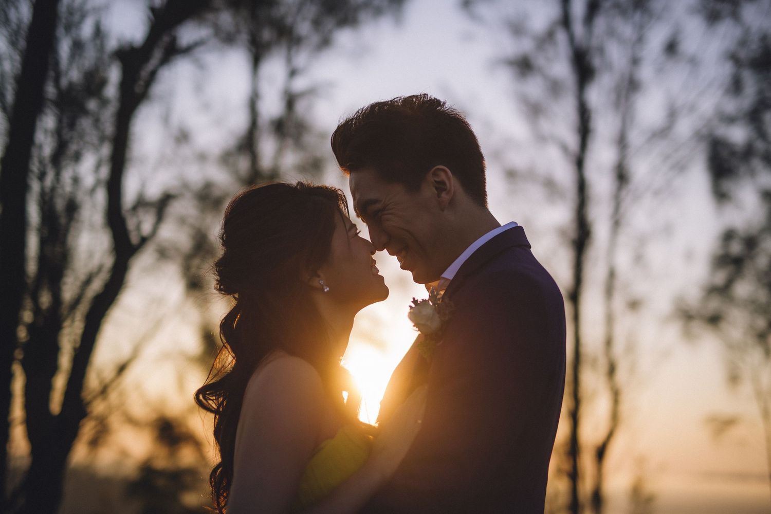 Silhouettes of a couple embracing against a golden sunset with trees in the background.