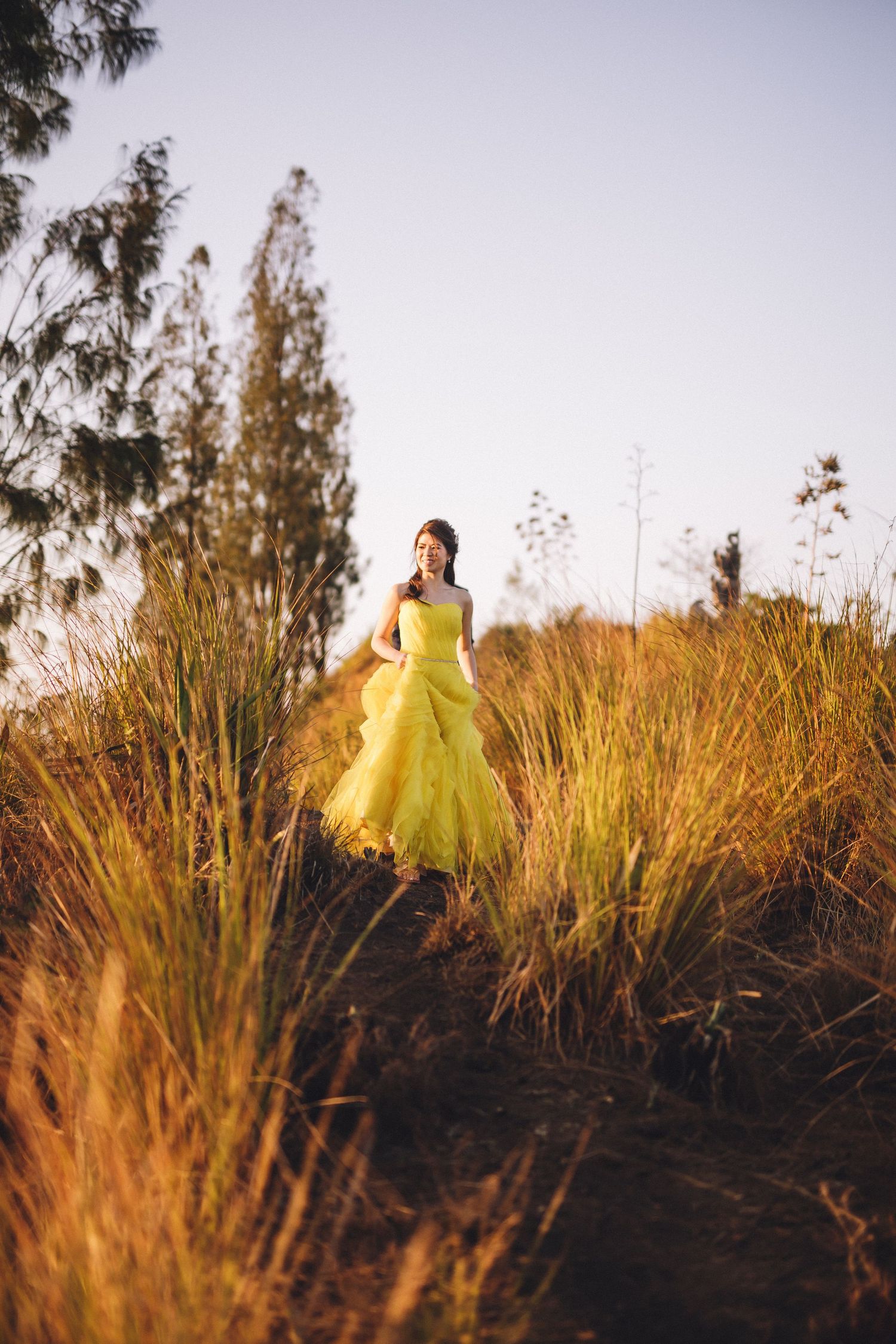 Woman in a bright yellow dress standing in tall grass during golden hour.
