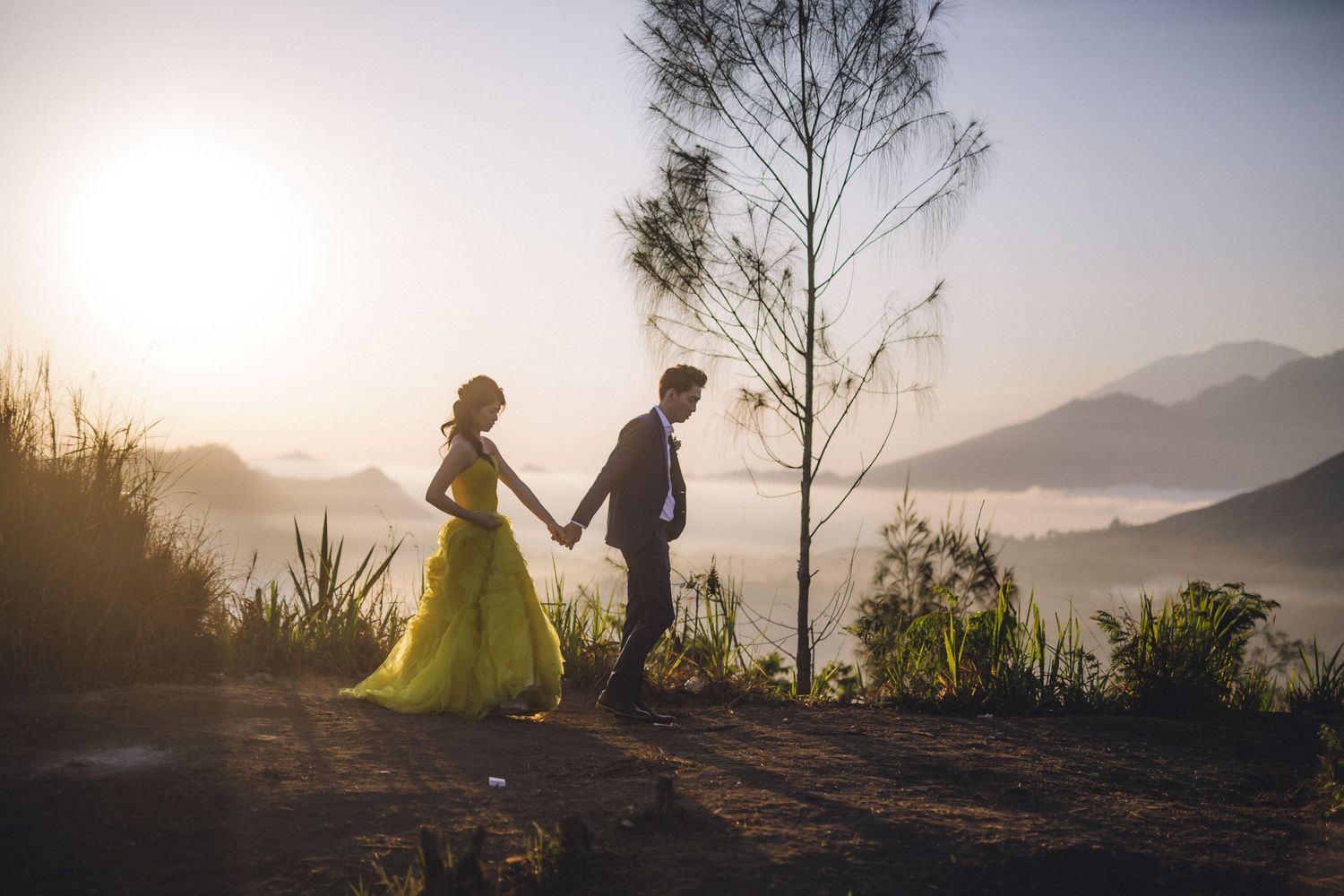 Couple walking along mountain ridge during golden hour with dramatic sky.