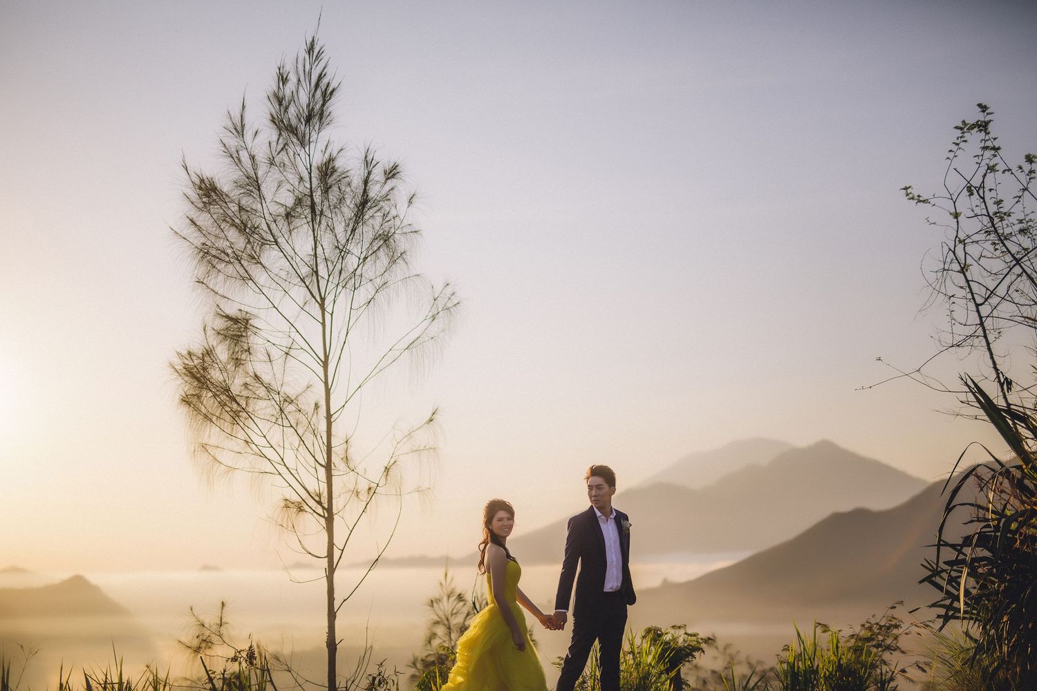 Couple walking hand in hand on mountain path during sunset.