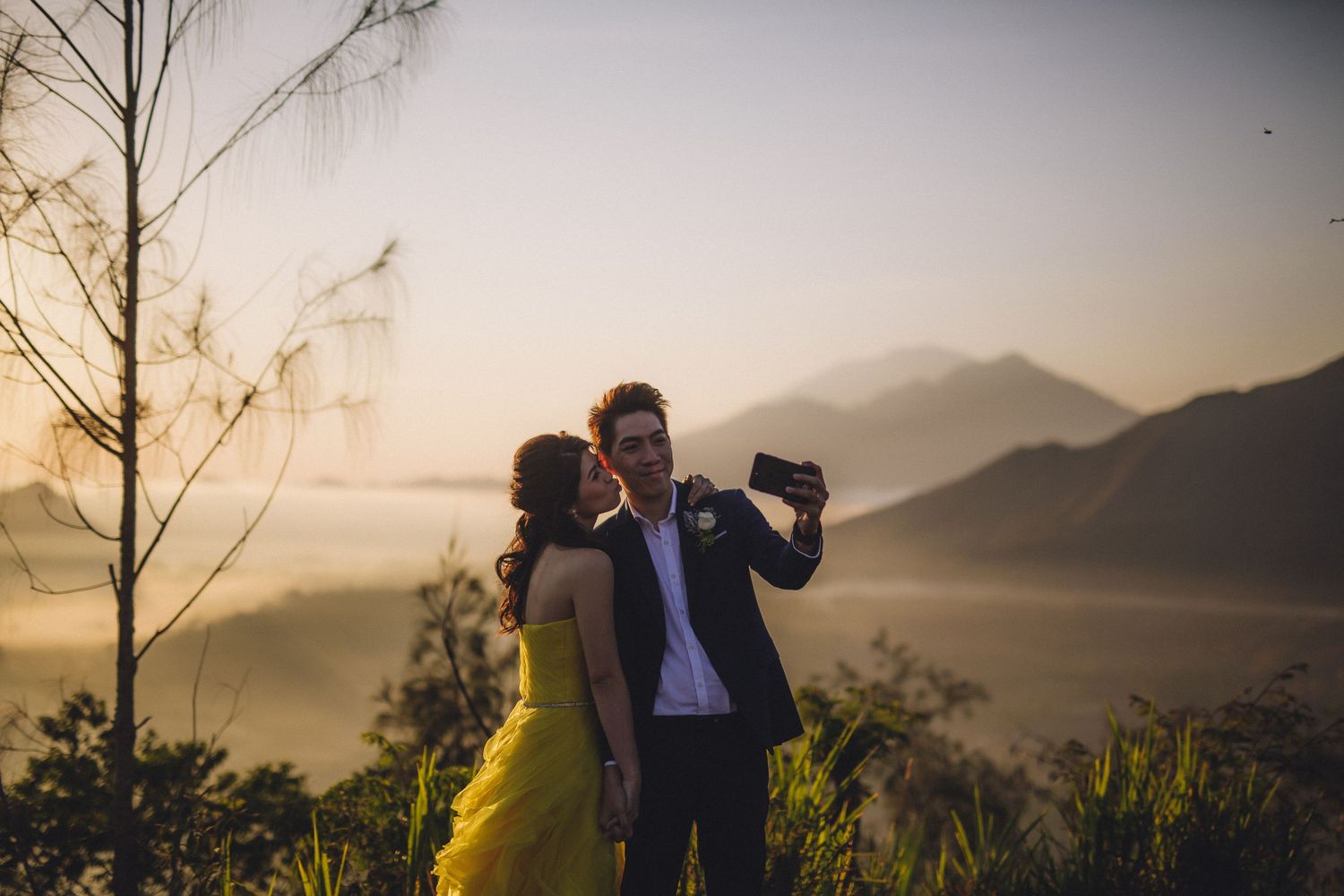 A couple shares an intimate moment against a misty mountain backdrop during sunset.