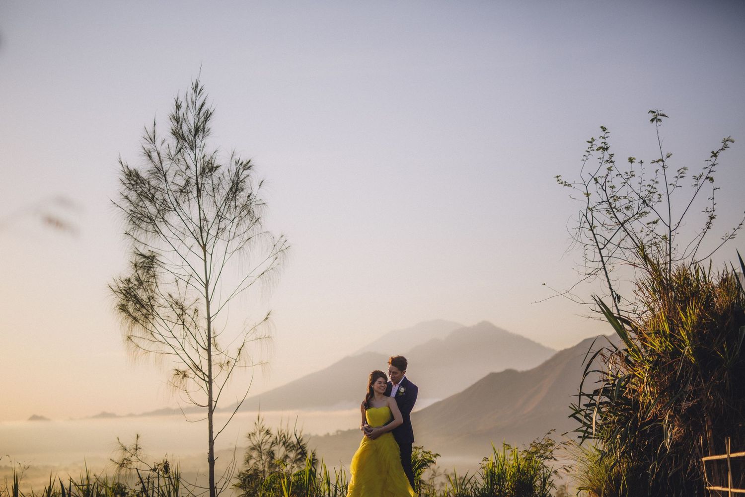 A romantic silhouette of a couple against mountains and trees during sunset.