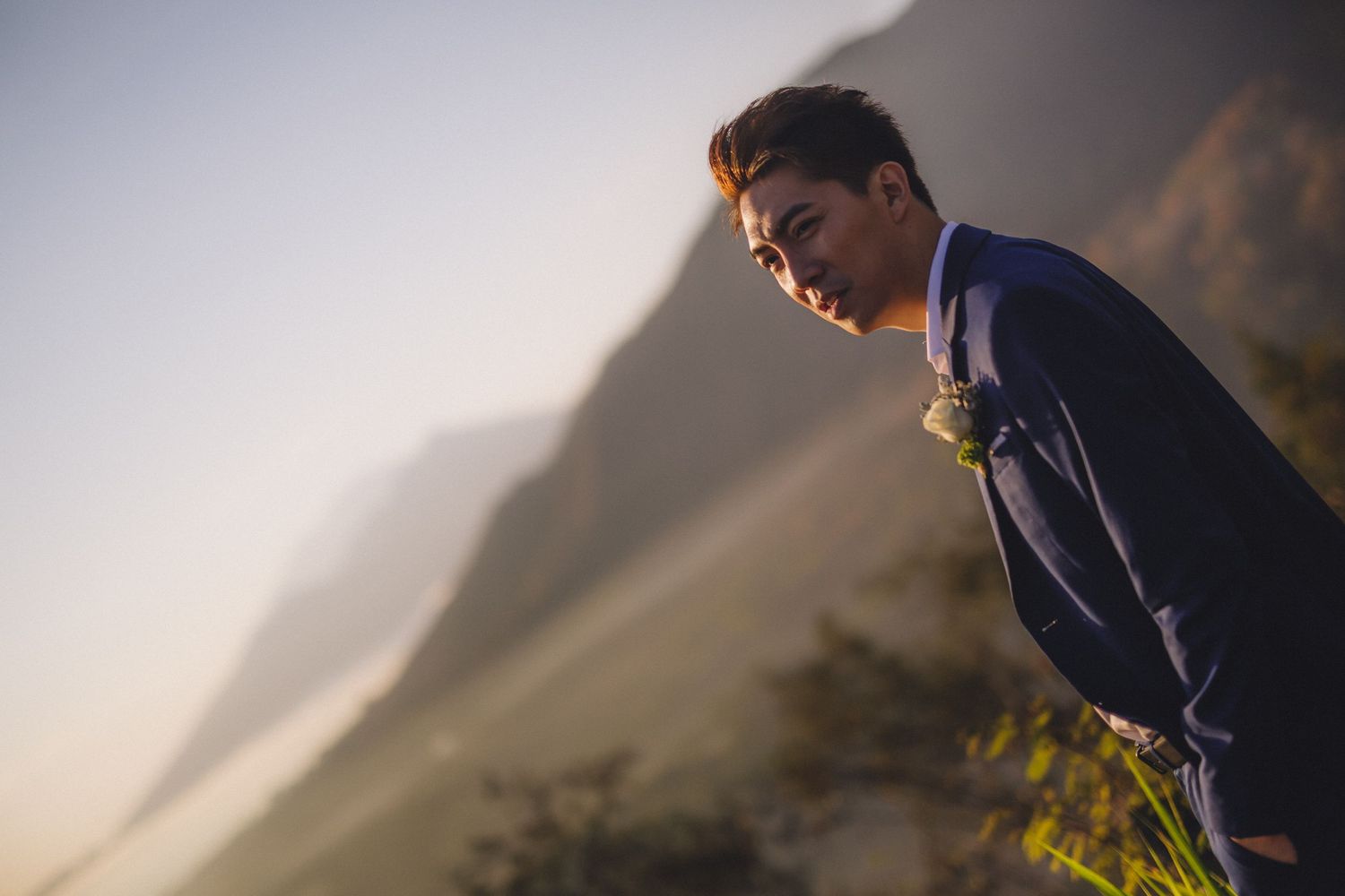 A person in a navy suit gazes thoughtfully at the mountain landscape during golden hour.