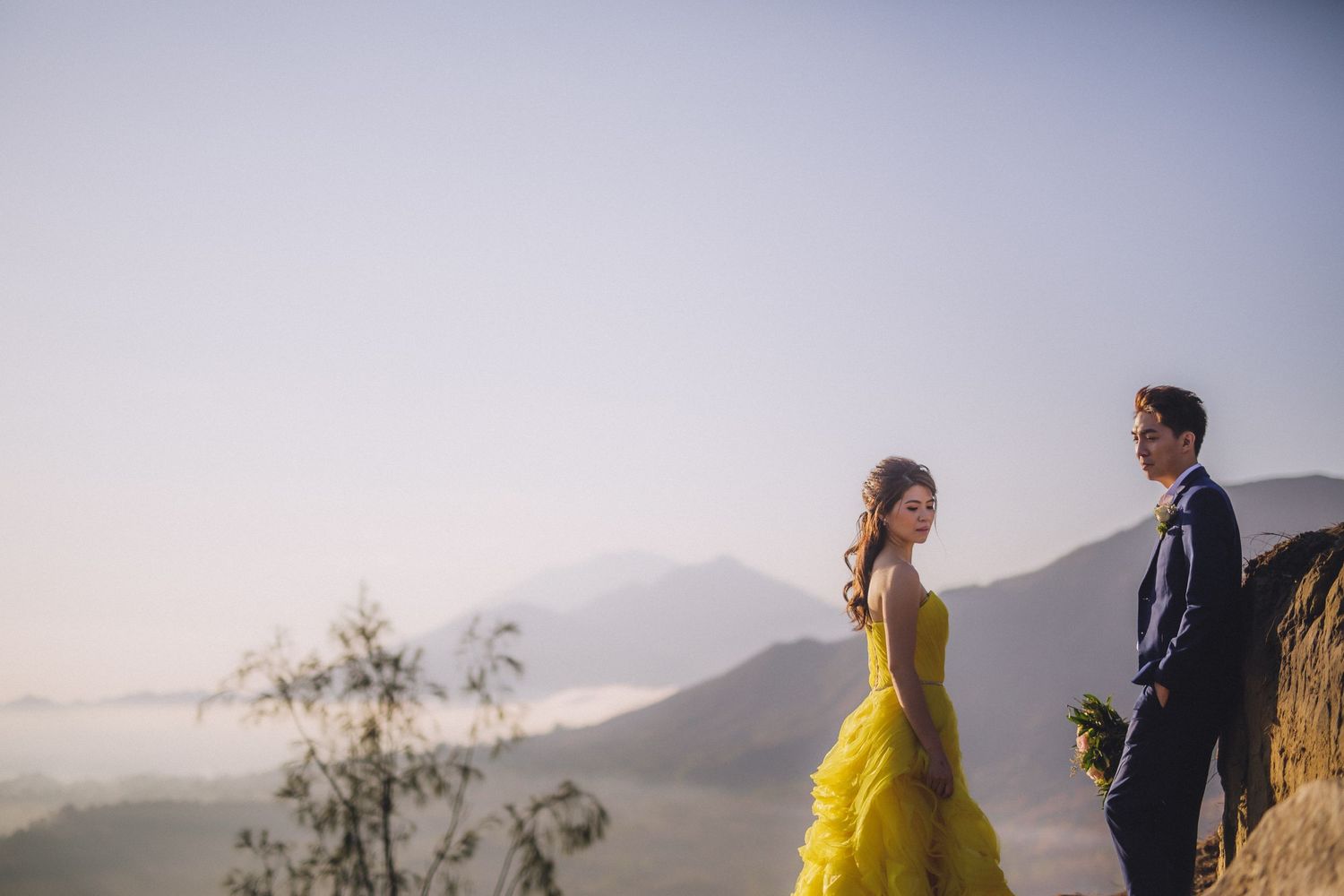 A couple in yellow and navy stands against a misty mountain backdrop.