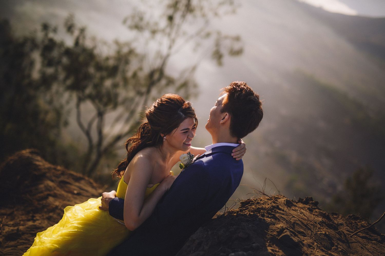 A romantic embrace between a couple in formal wear on a mountain cliff.