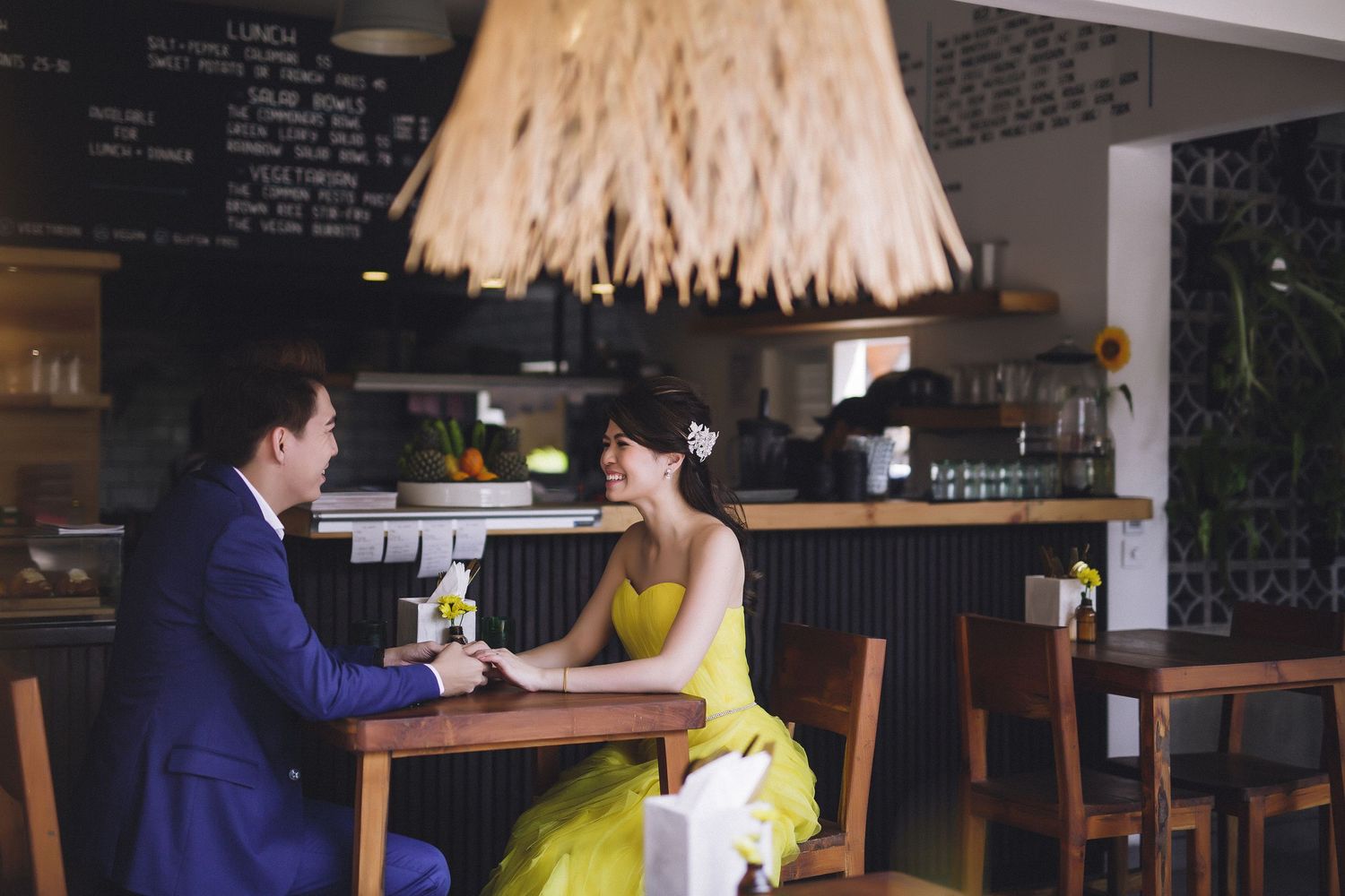 A couple in formal attire shares a moment at a rustic cafe with pendant lighting.