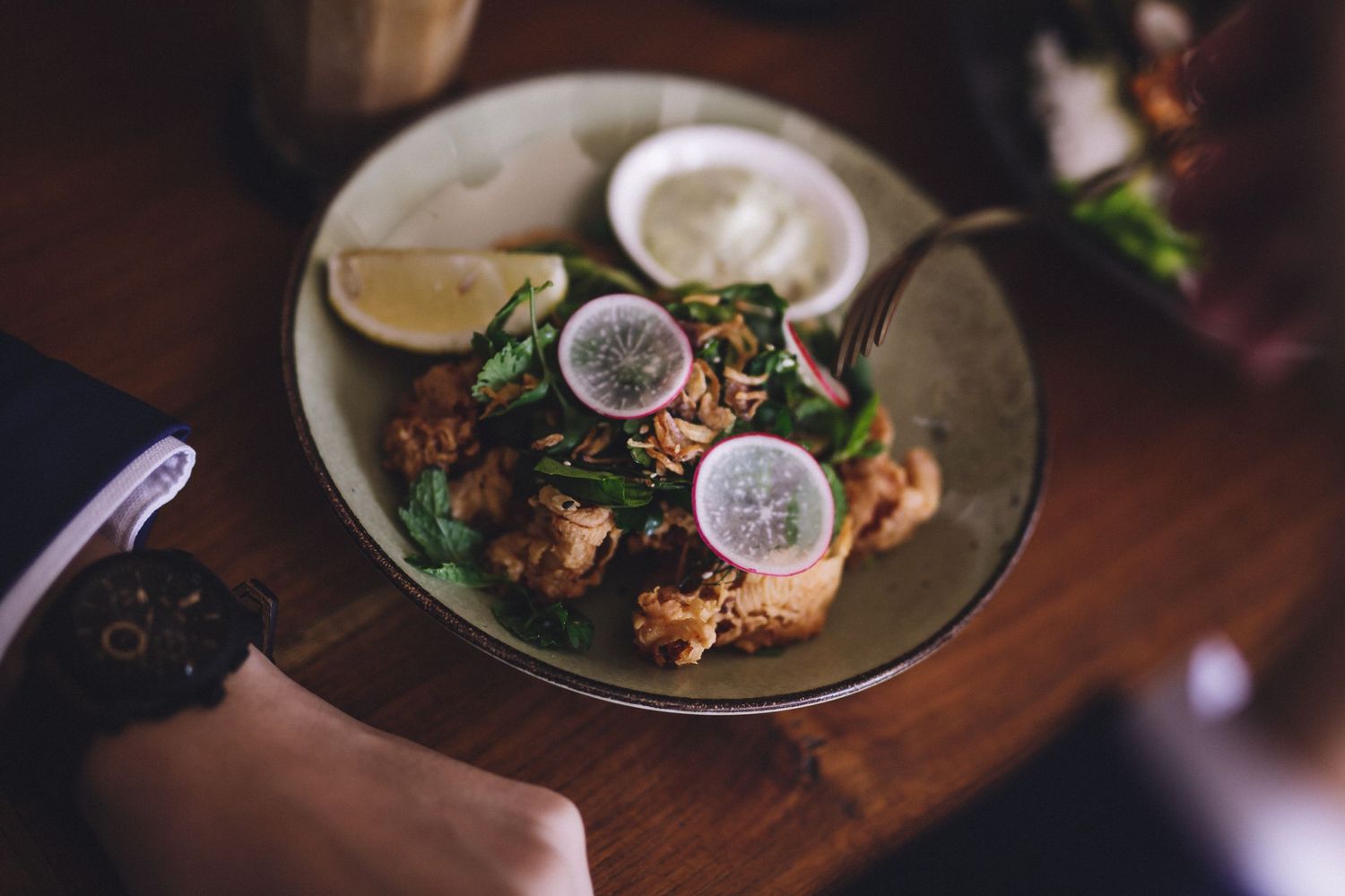 Multiple plates of garnished food served on a wooden restaurant table.