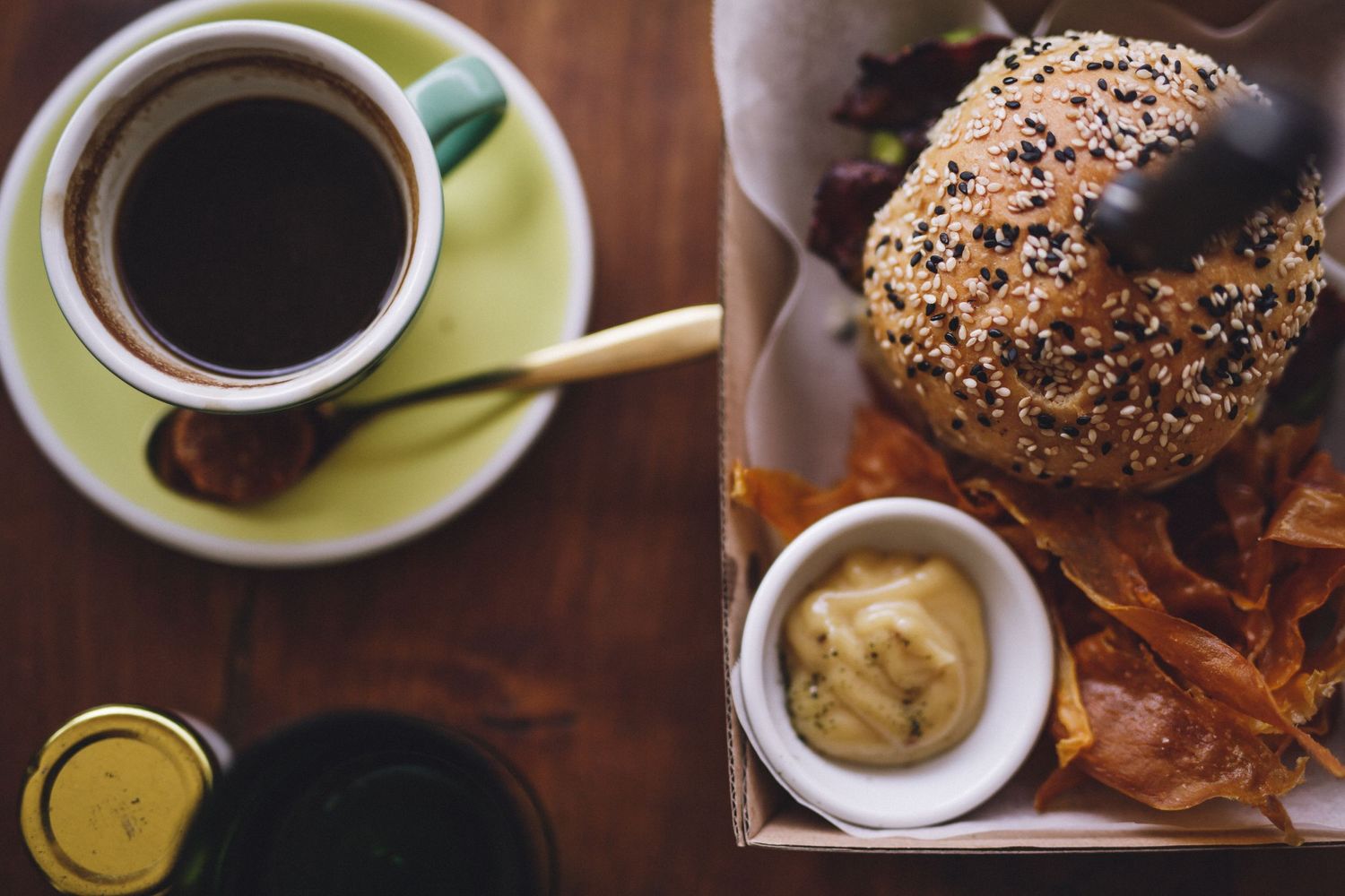 Coffee cups and food items including a seeded bun arranged on wooden surface.