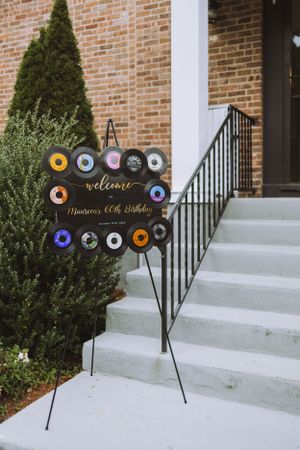Birthday party welcome sign made from vinyl records mounted on steps with brick background.